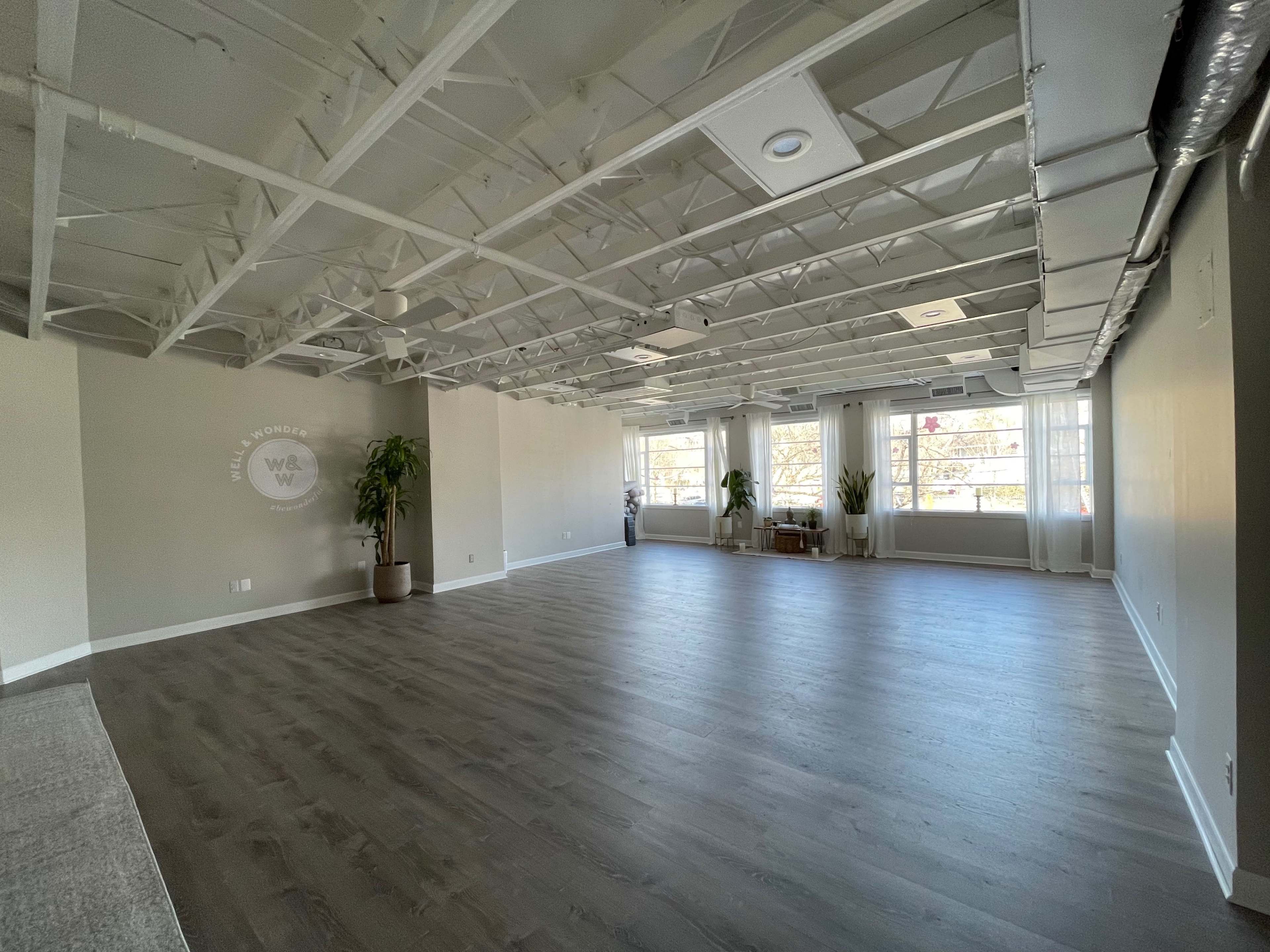 A spacious, empty interior room with large windows and exposed ceiling beams.