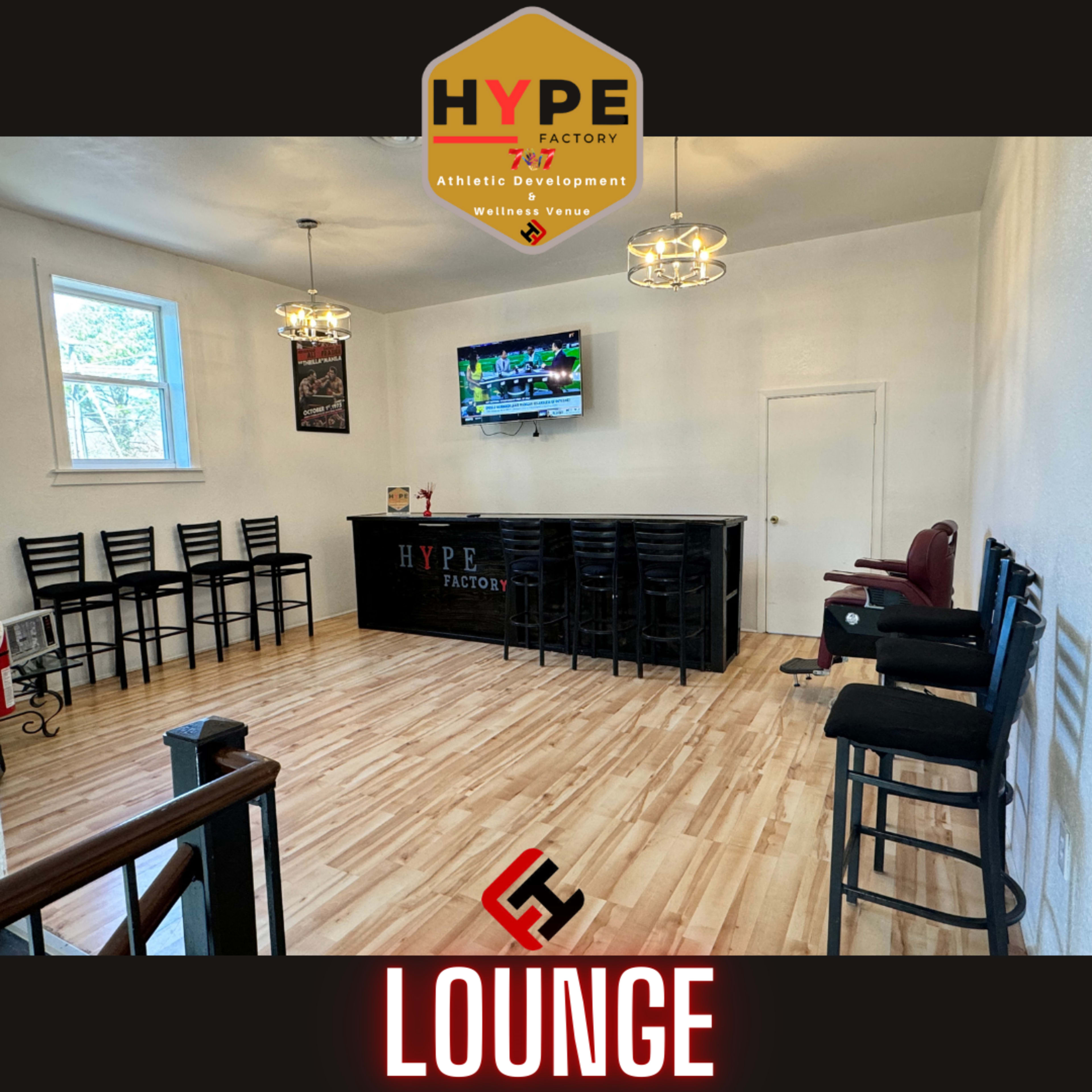 A spacious lounge area with a bar, high stools, a large TV on the wall, and wooden flooring.