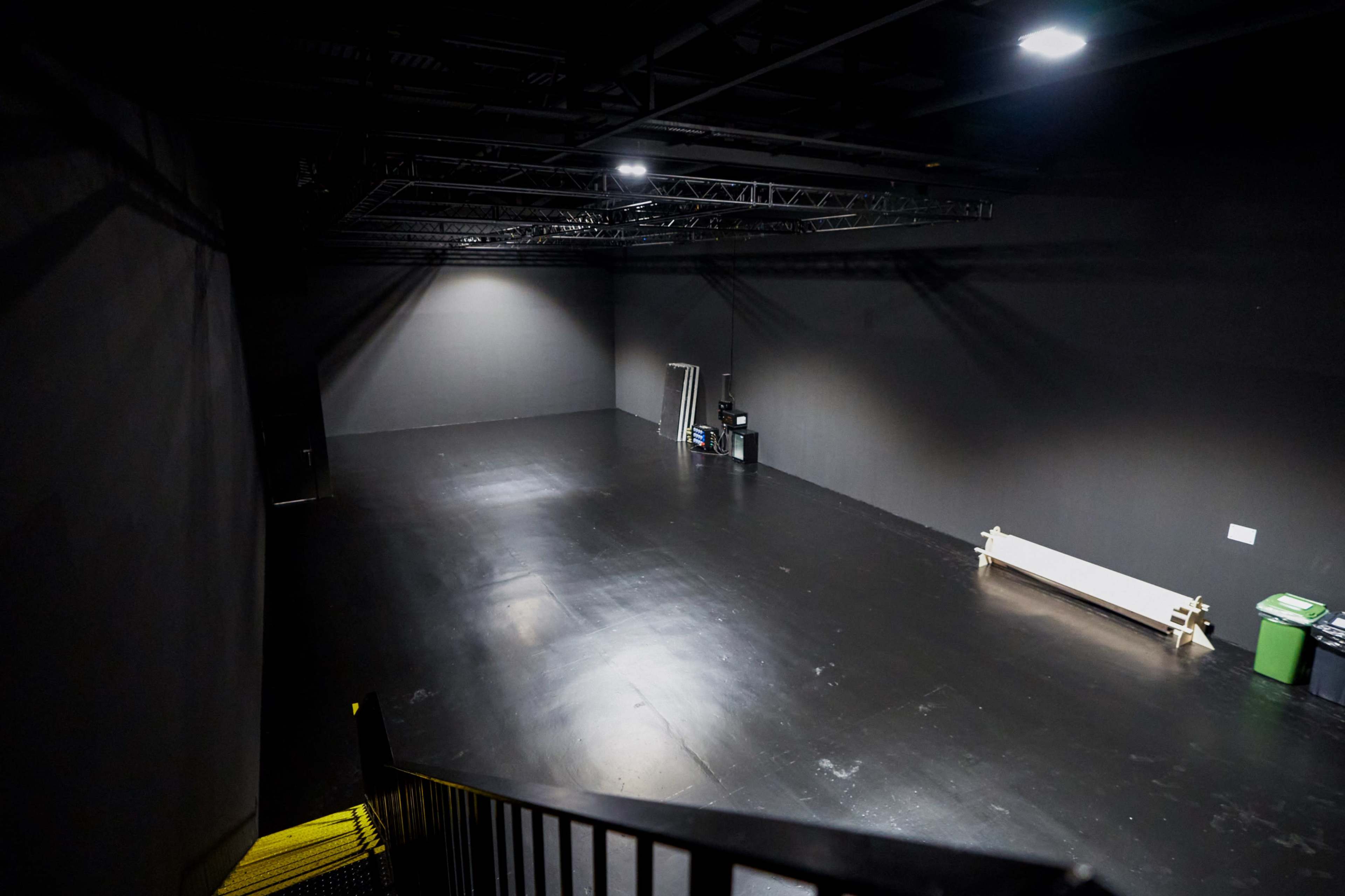 The image shows an empty black studio space with a smooth floor, dim lighting, and minimal equipment near the back.