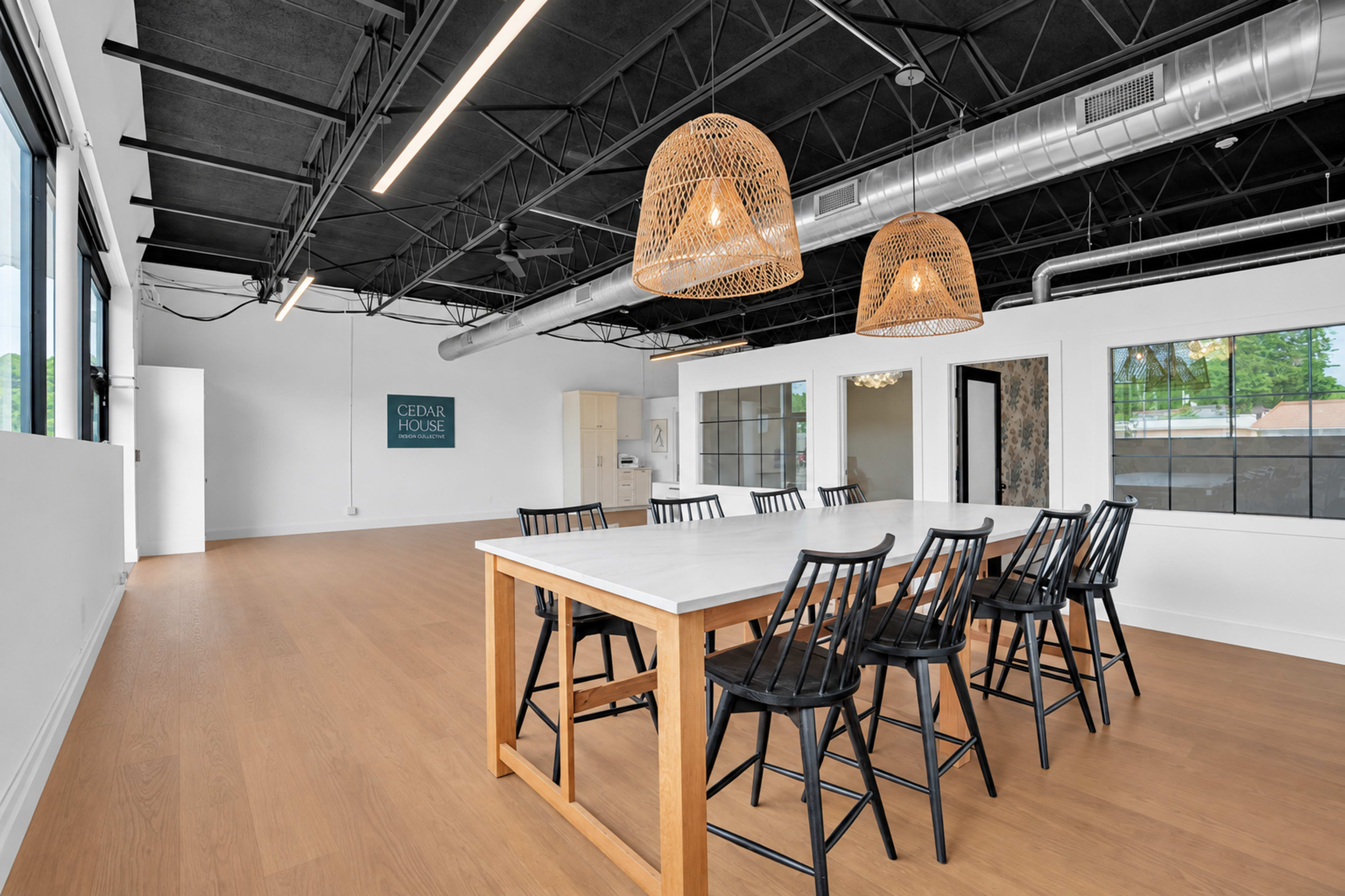 The image shows a spacious modern interior with a large table surrounded by black chairs, illuminated by two woven pendant lights.