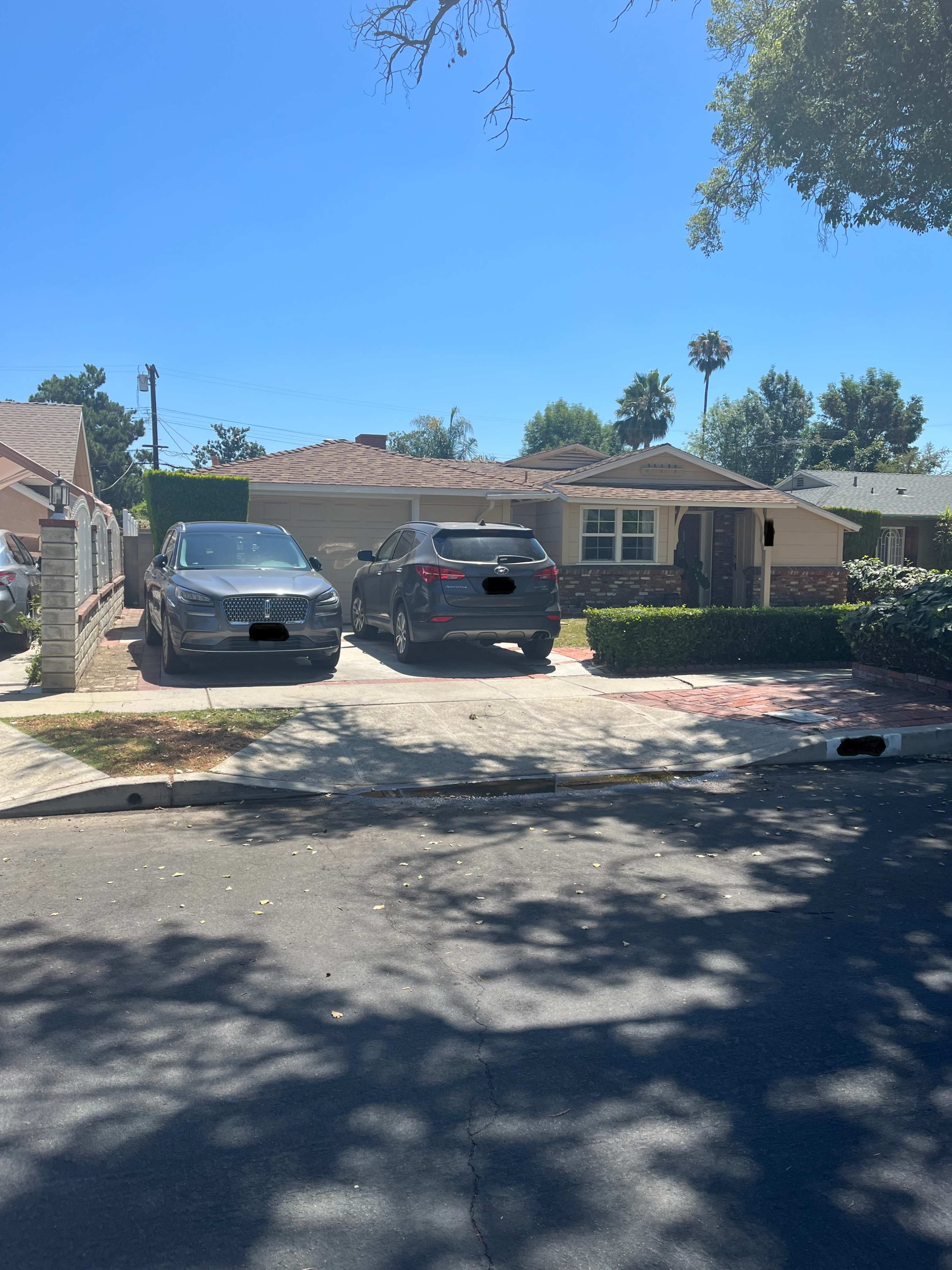 Two cars parked in the driveway of a single-story house with a lawn and palm trees in the background.