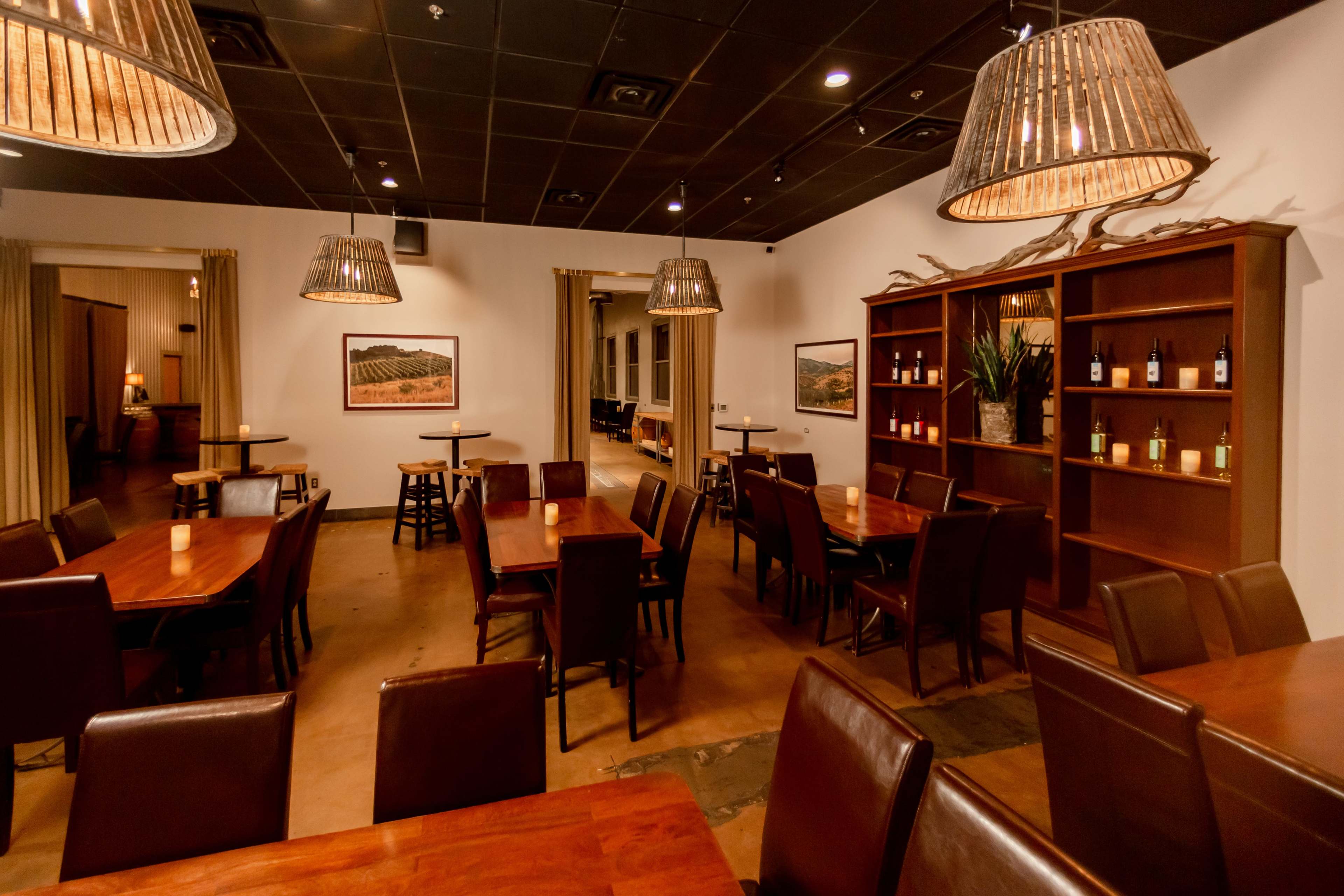 A spacious restaurant interior with wooden tables, leather chairs, and soft lighting from woven pendant lamps.