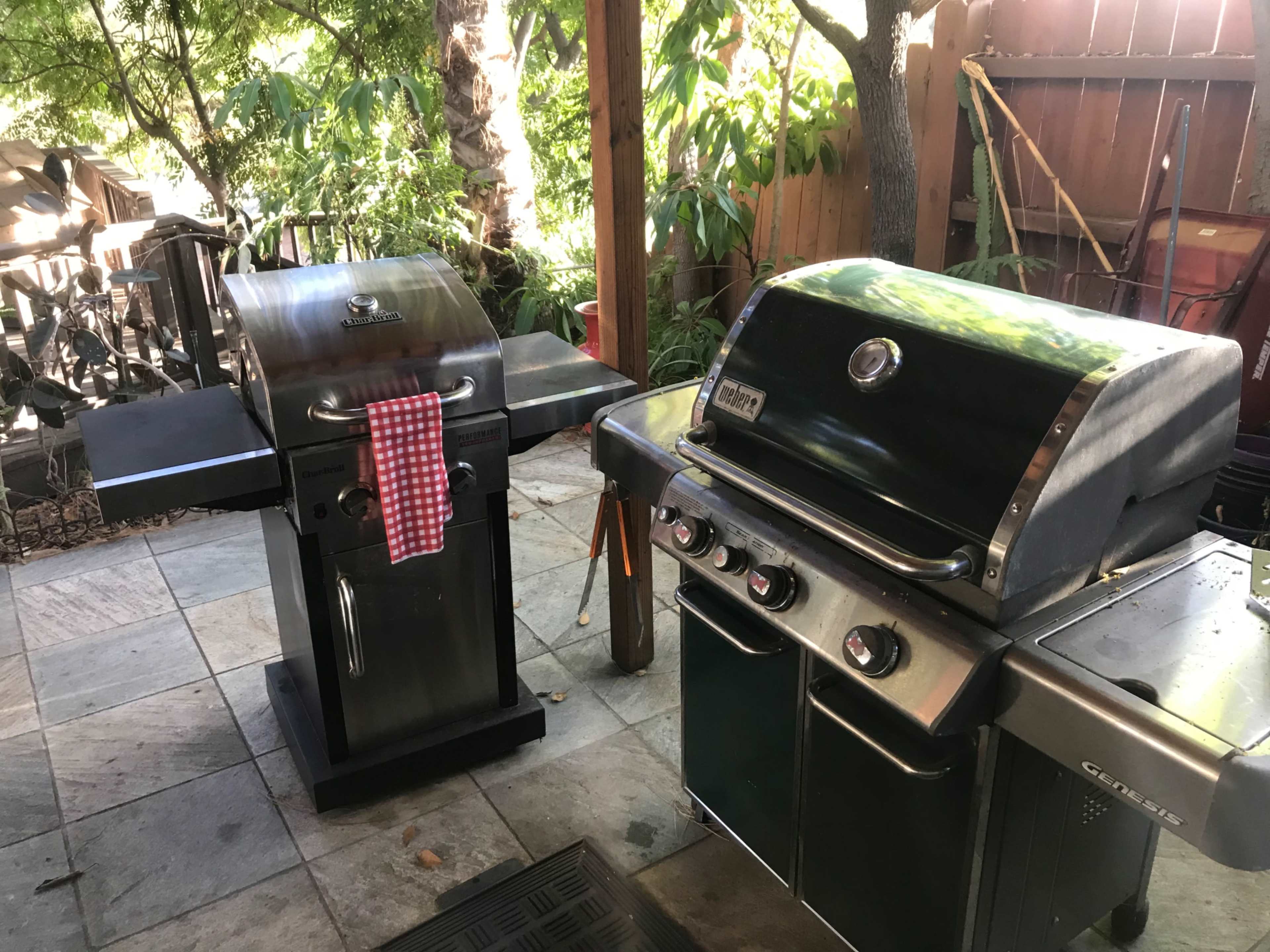 Two outdoor grills placed on a patio, with a red-checkered towel hanging on one of them.