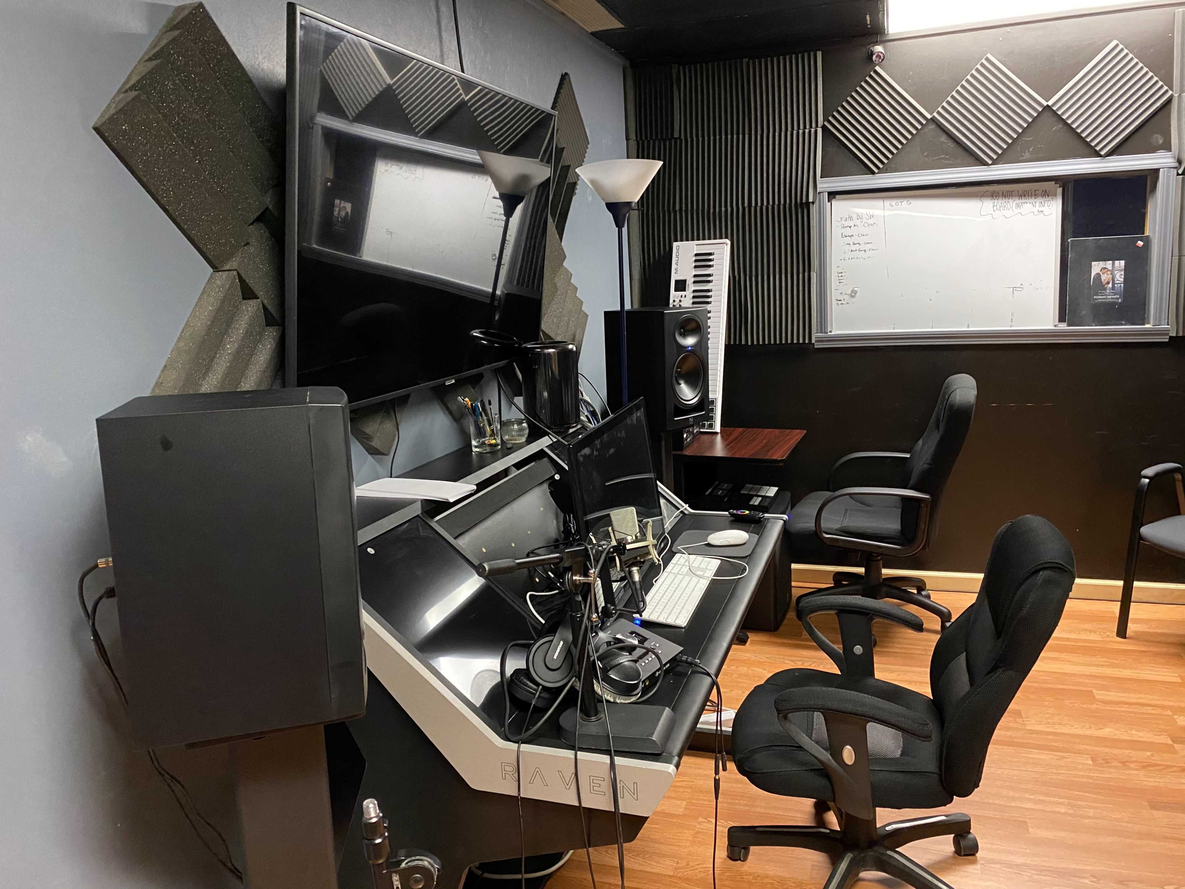 A recording studio equipped with acoustic panels, a large monitor, a computer setup, and seating arranged for music production.