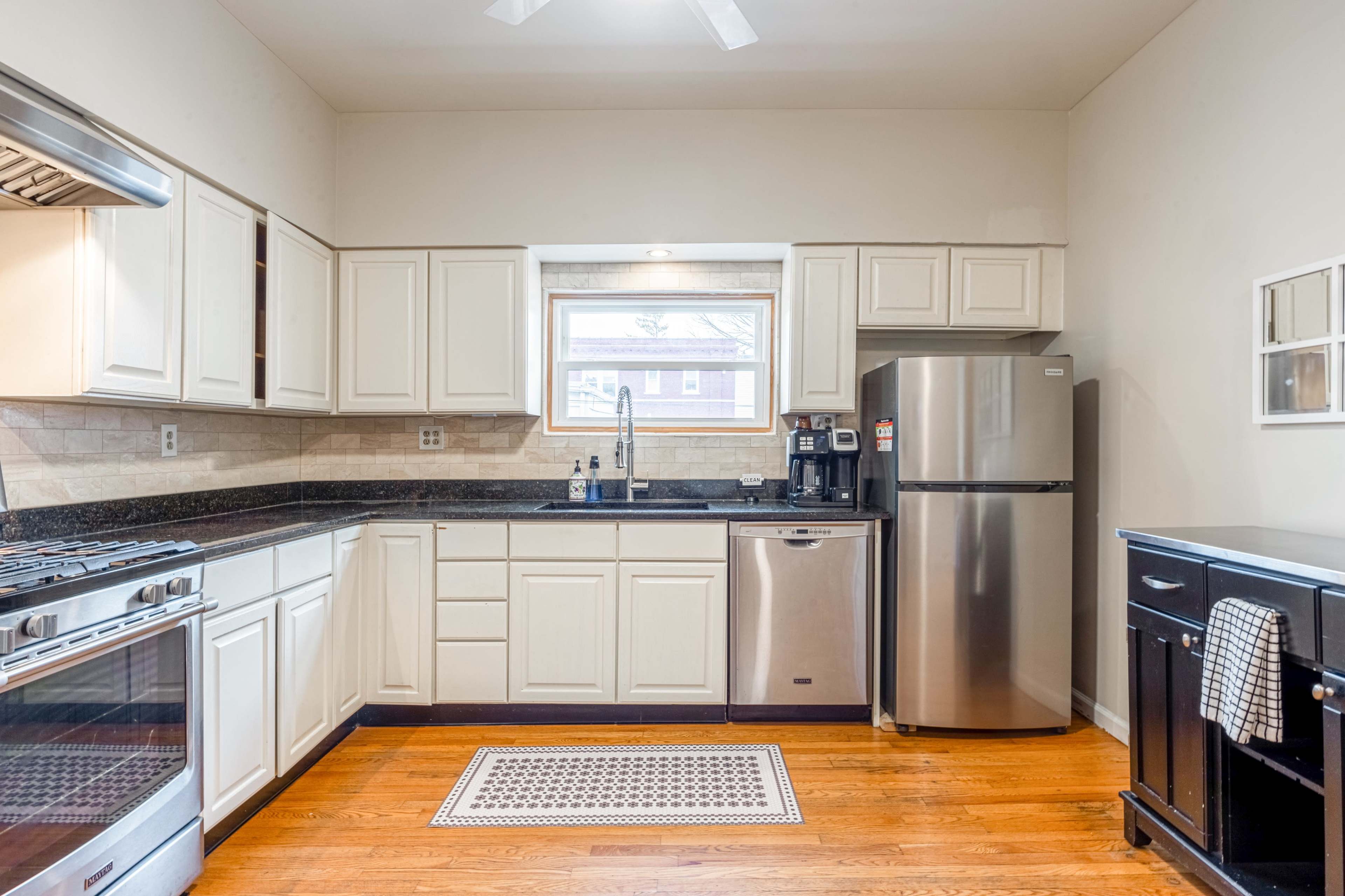 A modern kitchen with white cabinets, stainless steel appliances, and hardwood flooring.