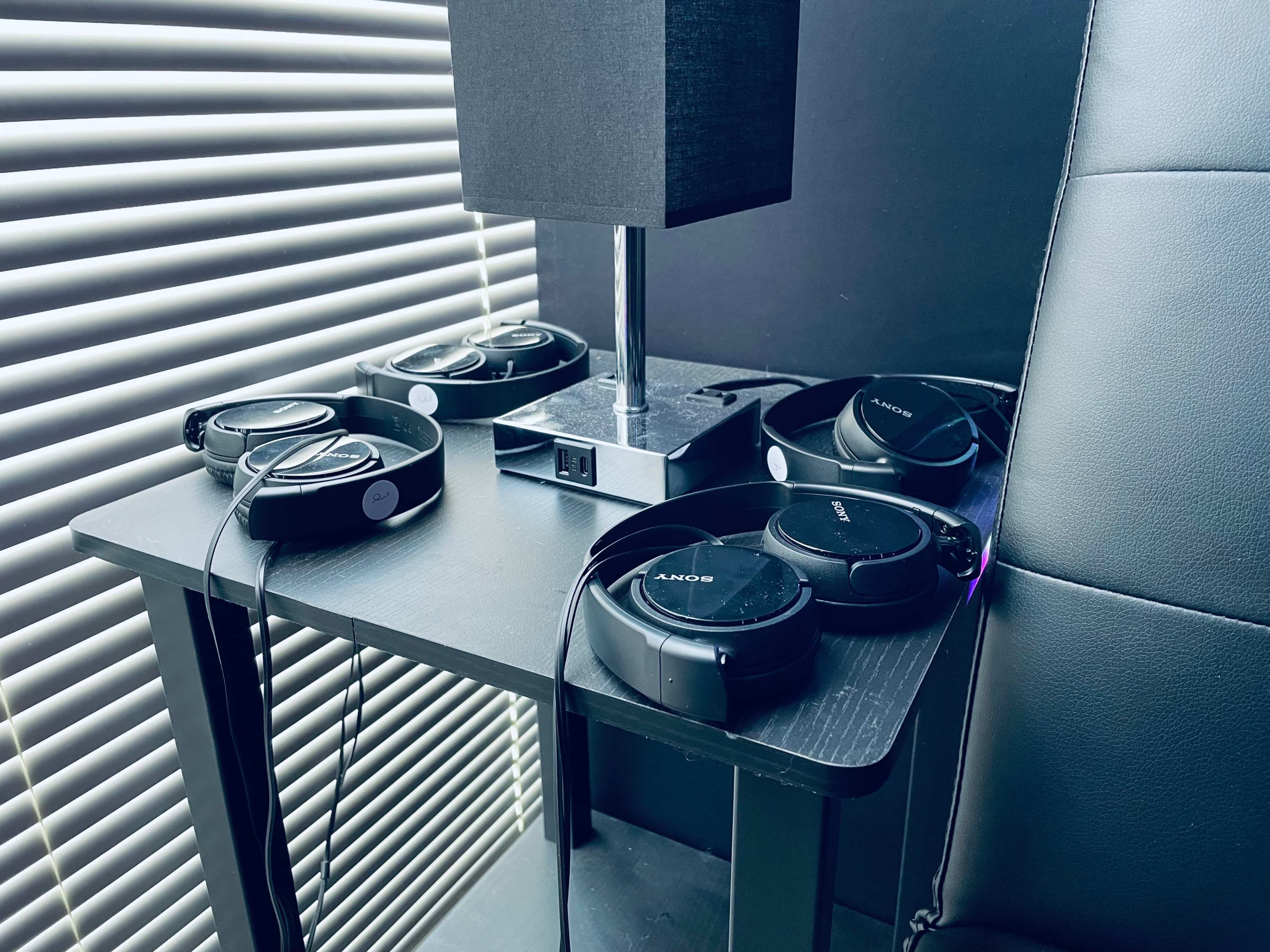 A table with a lamp and multiple pairs of headphones resting on it.