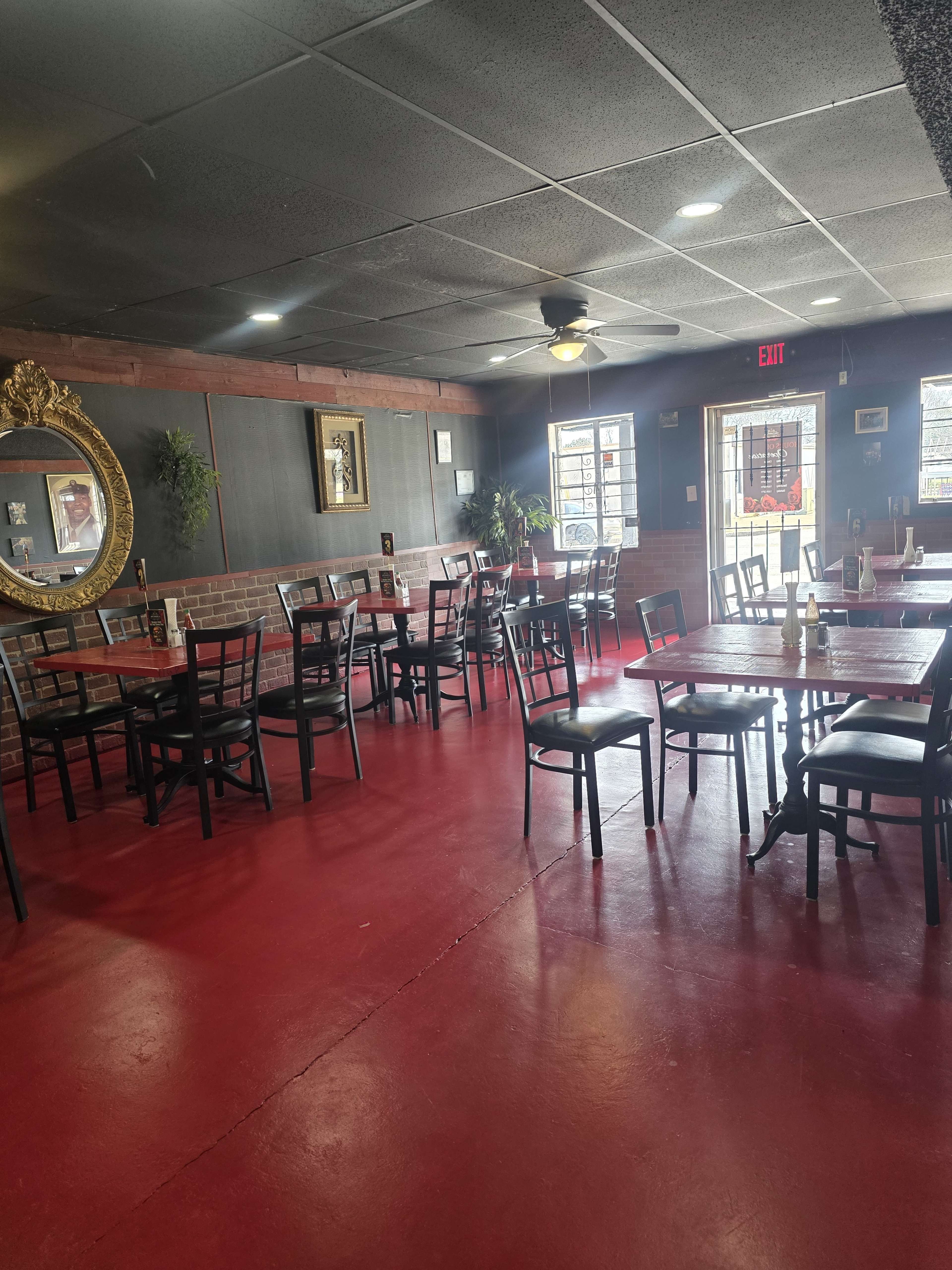 The image shows an empty restaurant interior with red floors, black tables and chairs, and a large mirror on the wall.
