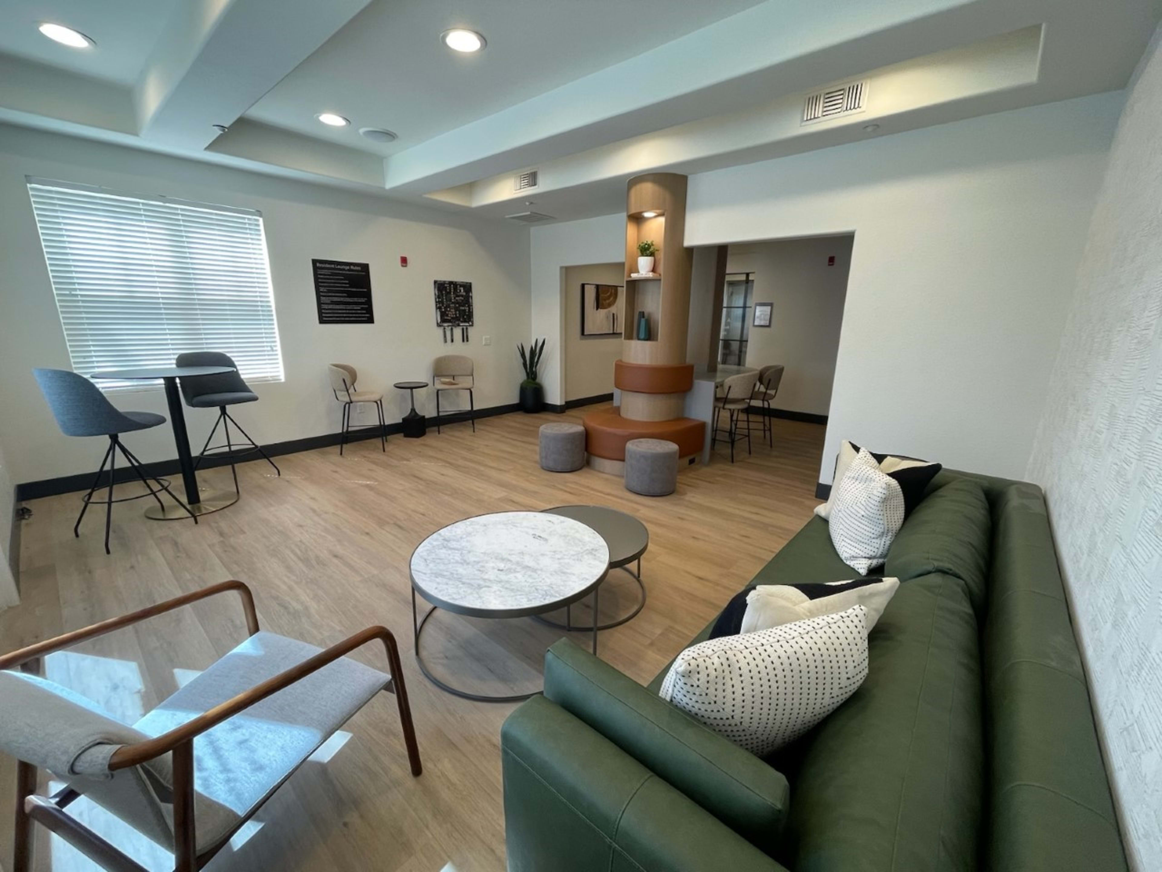 A modern lounge area featuring a green sofa, a marble coffee table, several chairs, and a small bar table.