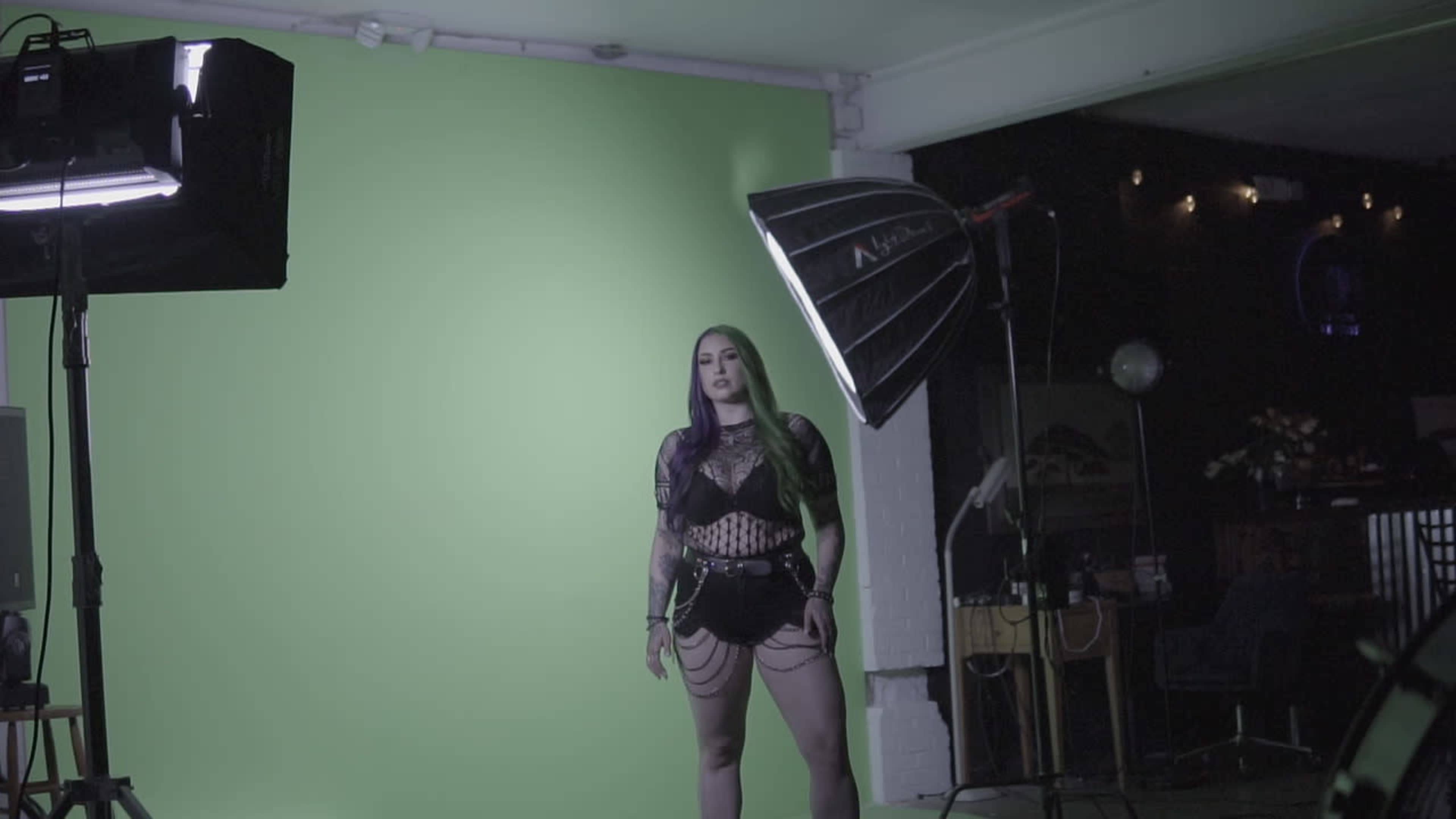 A model stands in front of a green screen with studio lighting and equipment arranged in the background.