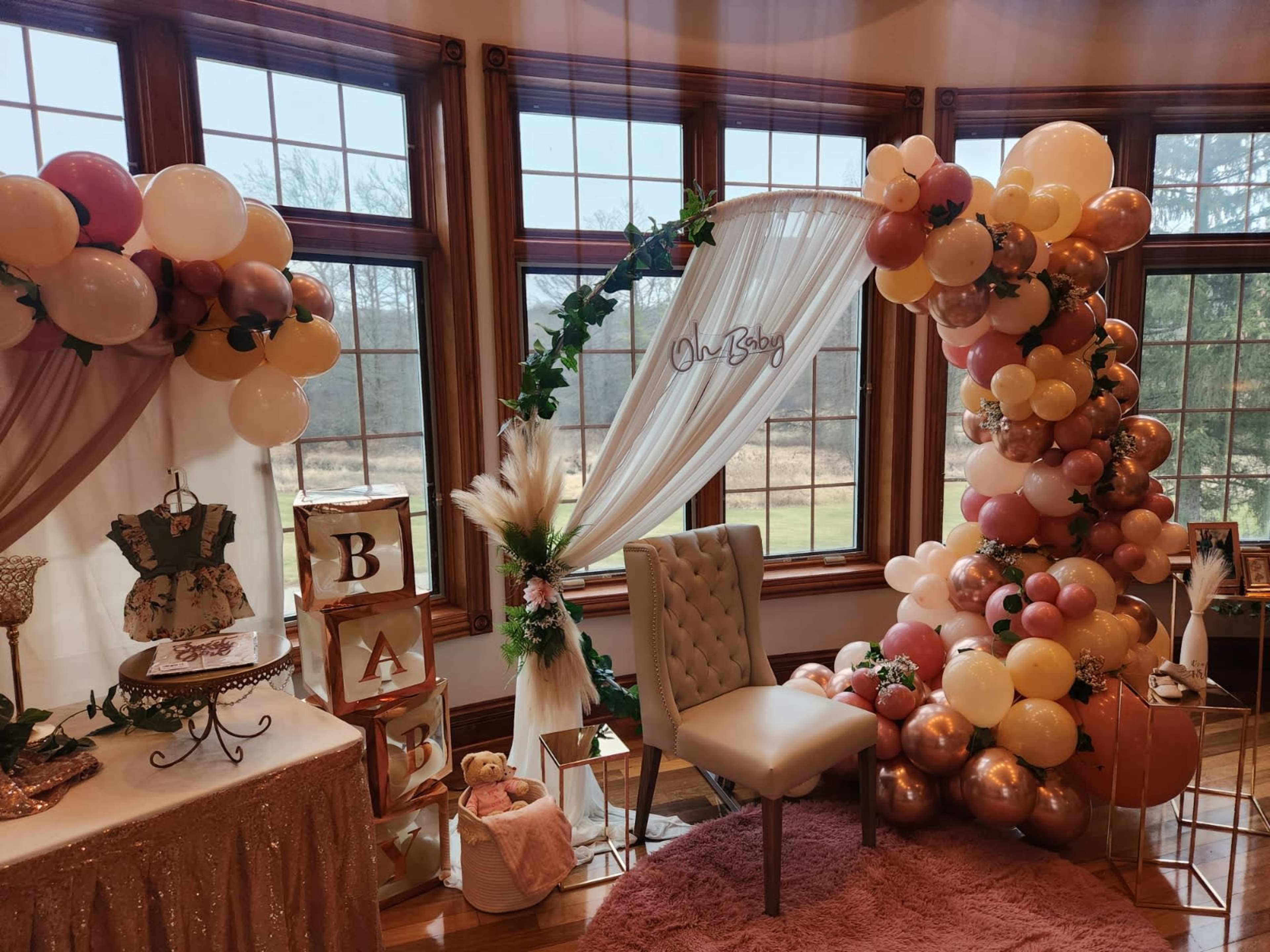 A decorated room with a backdrop of balloons, a small chair, and a table adorned with baby-themed decor for a celebration.