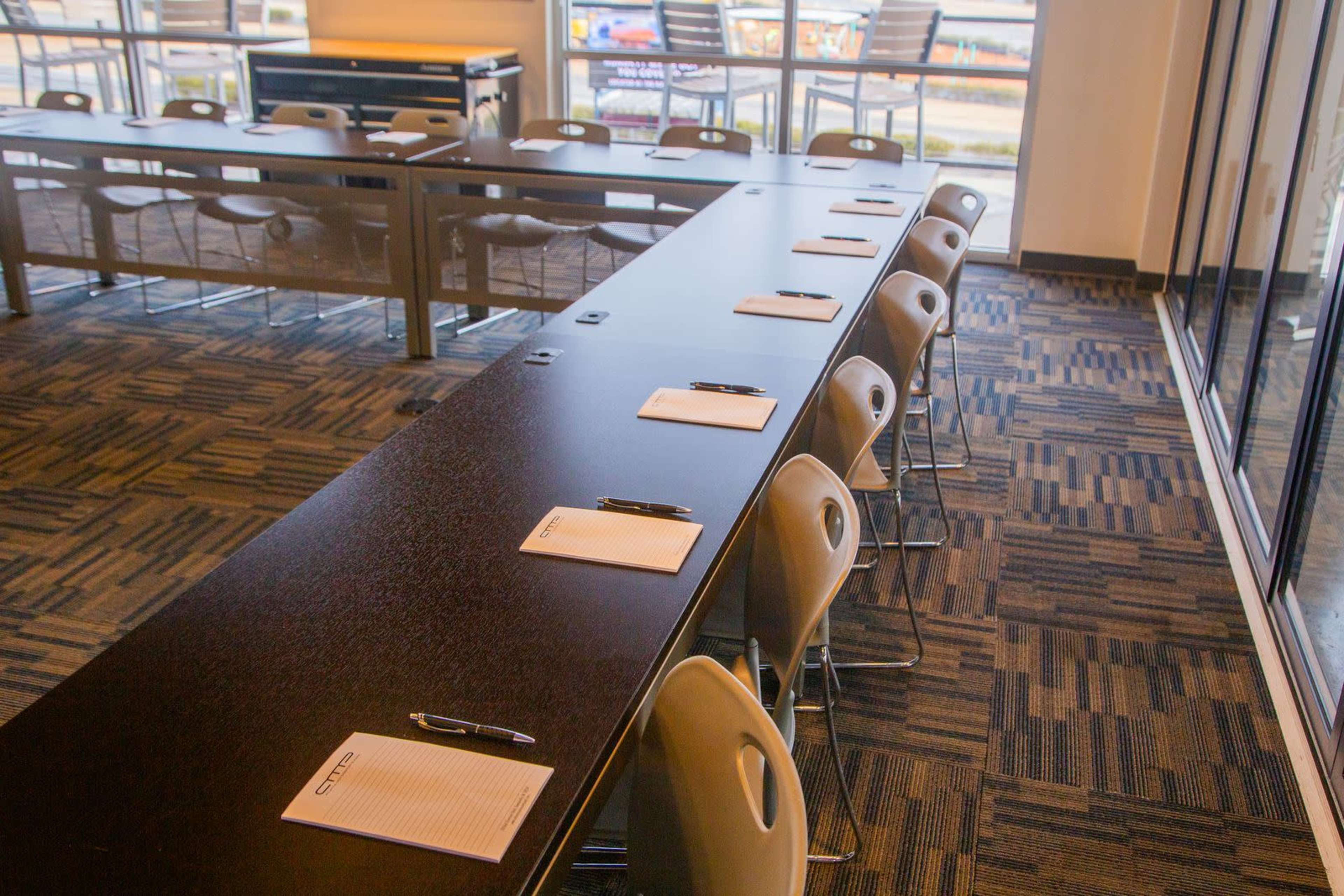 A long conference table is arranged with notepads and pens, situated in a modern meeting space with large windows.
