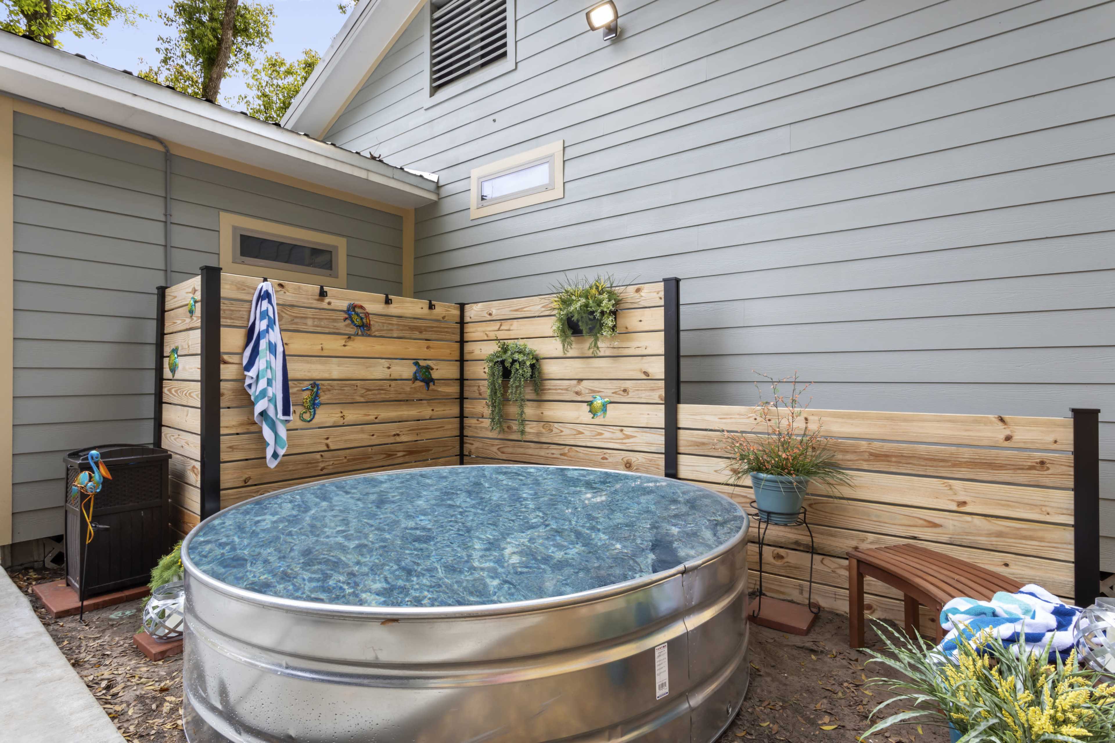 The image features a small outdoor area with a round, metallic above-ground pool enclosed by wooden fencing and decorated with potted plants.