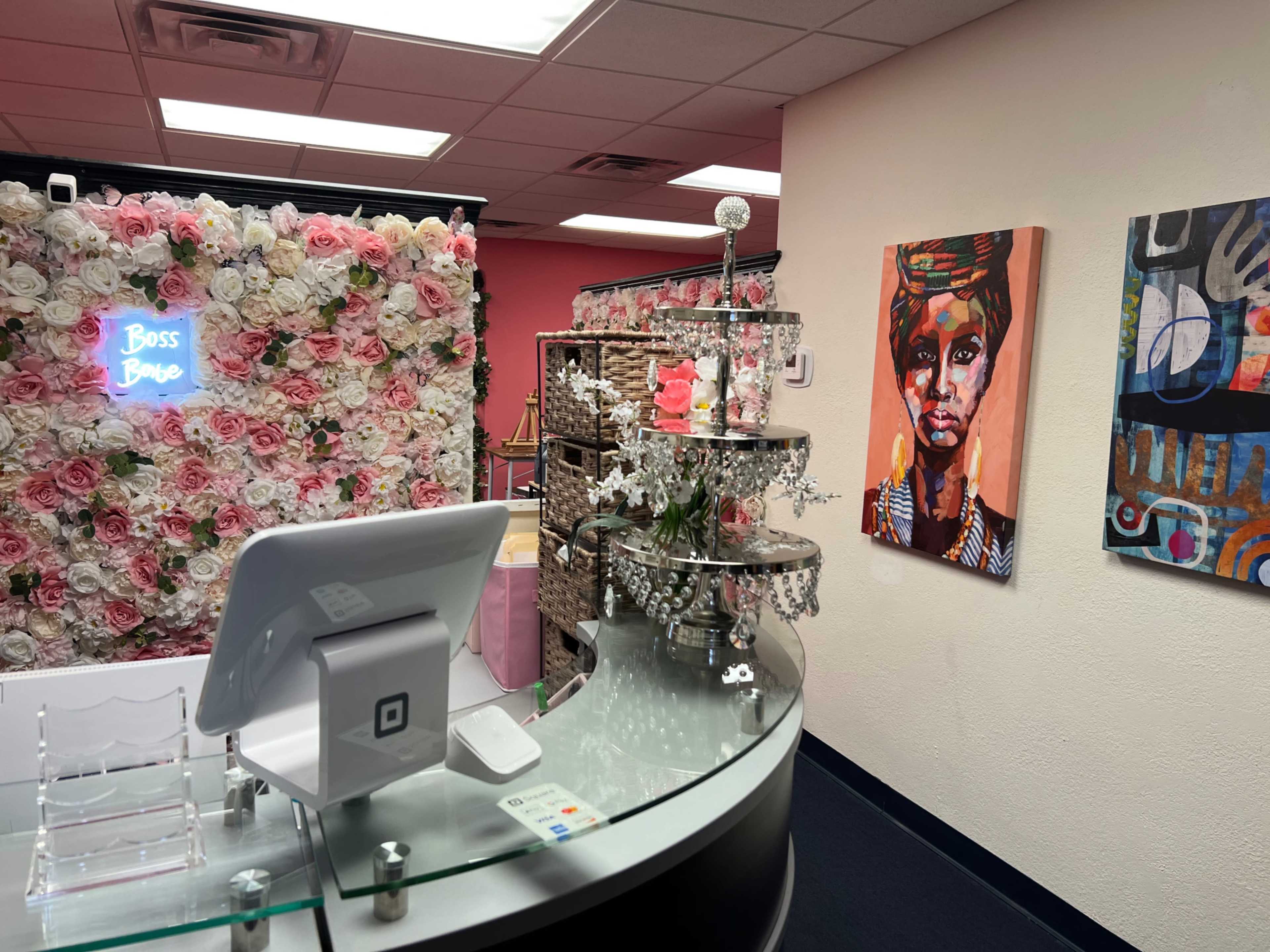 A retail space with a floral wall, a decorative display stand, and colorful artwork on the walls.