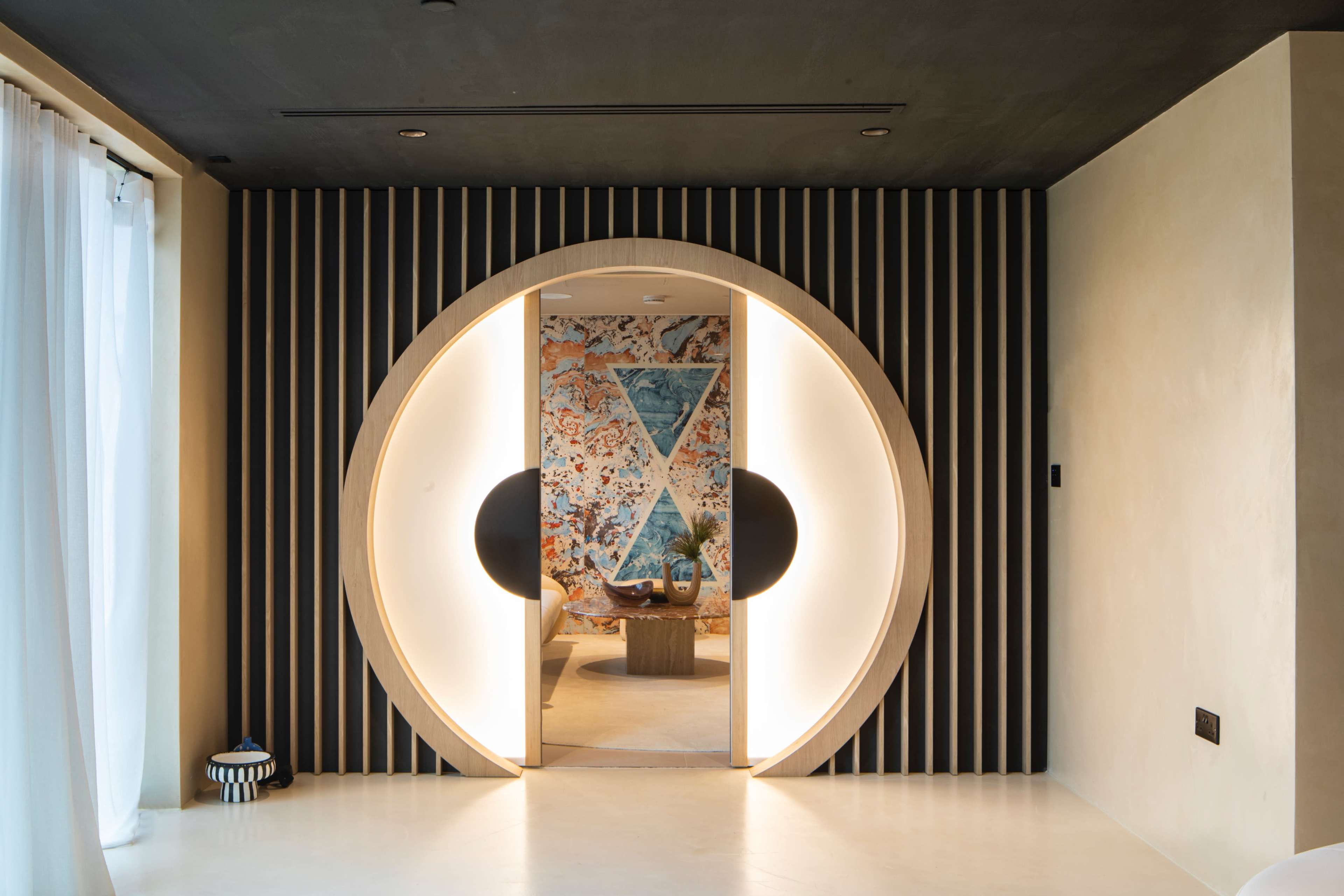 A modern interior with a circular doorway framed by black and white panels, leading into a room with colorful wall art.