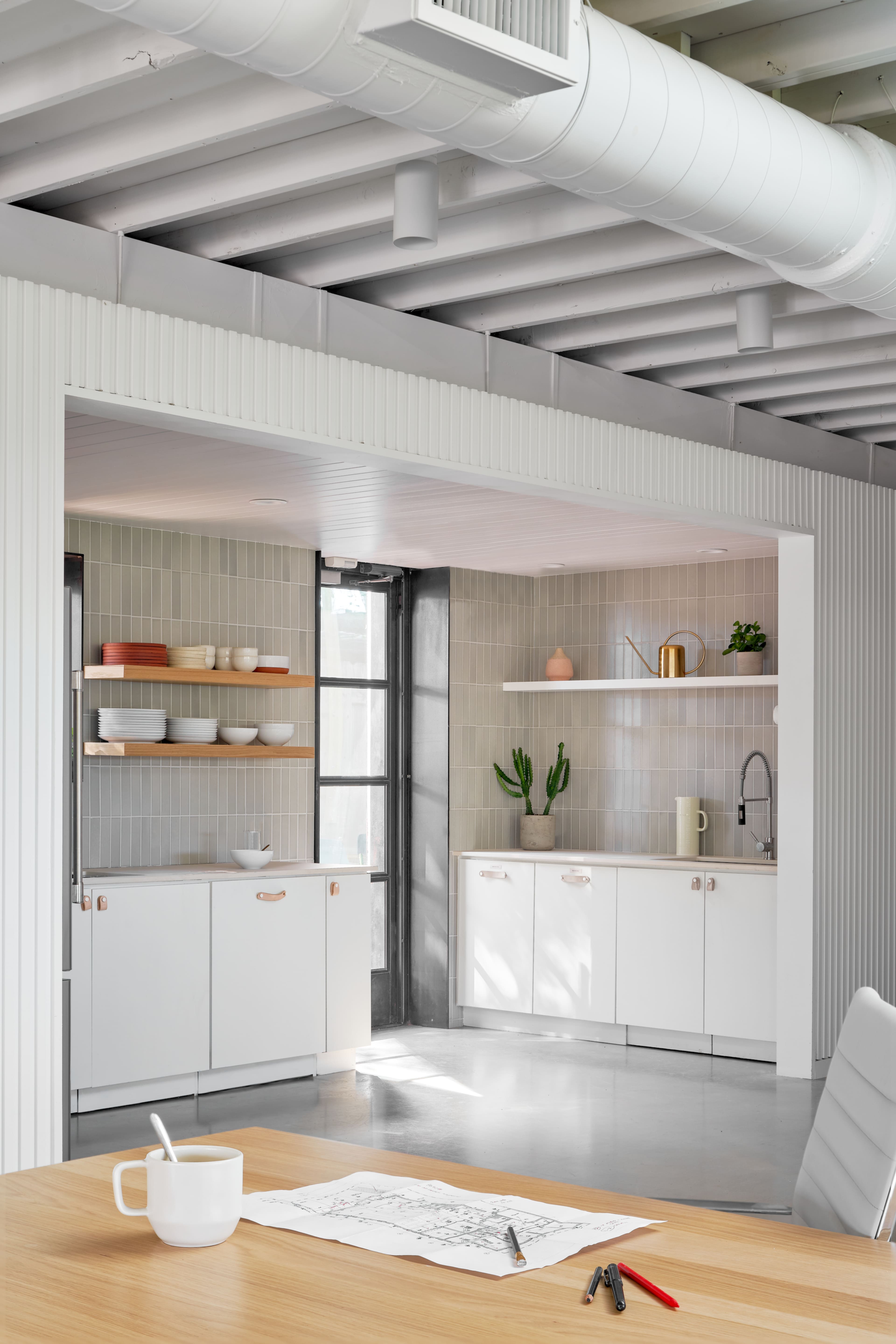 A modern kitchen features white cabinetry, open shelves displaying dishware, and a dining table with a sketch on it.