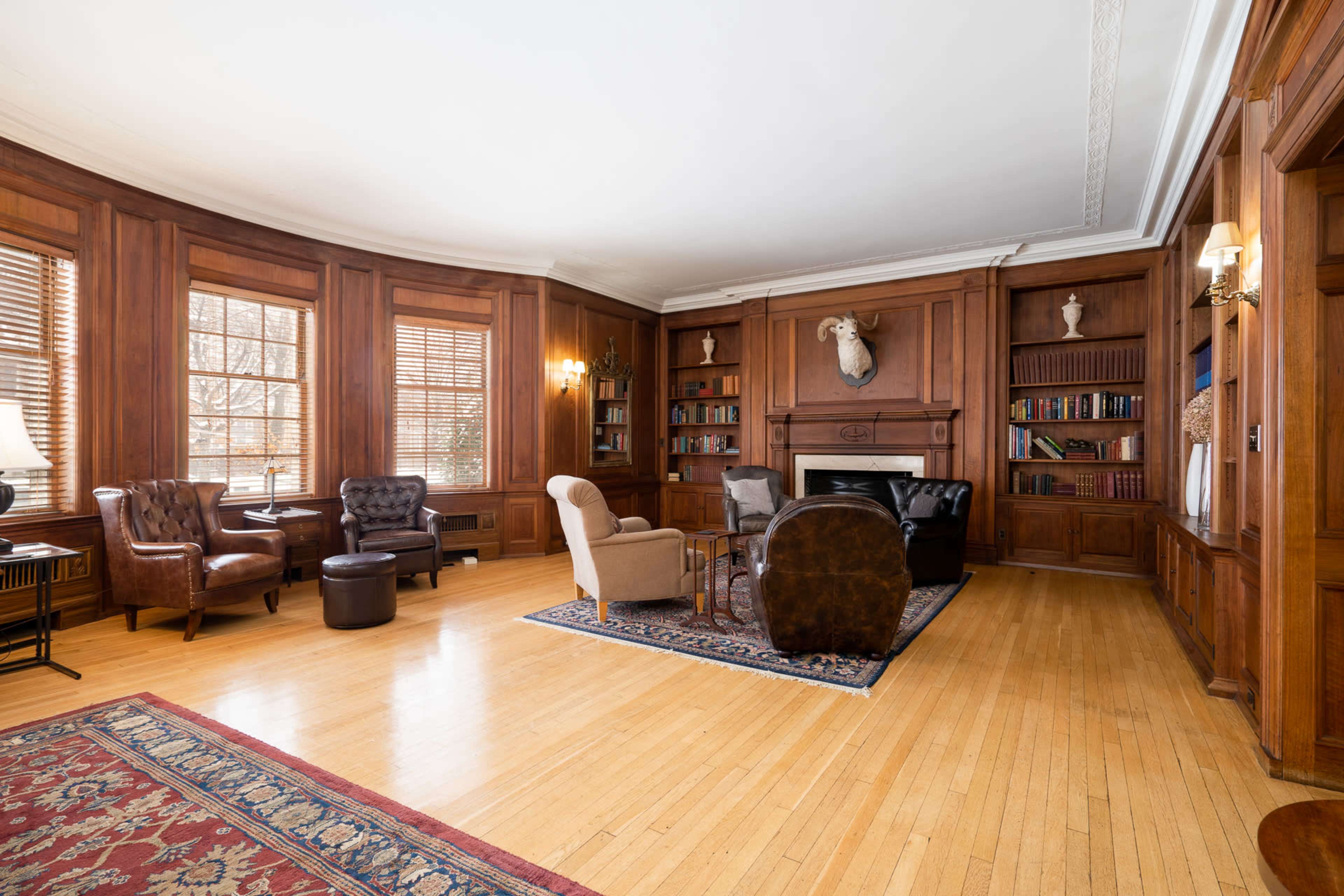 The room features wood-paneled walls, a fireplace, a variety of seating options, and a large area rug on hardwood flooring.
