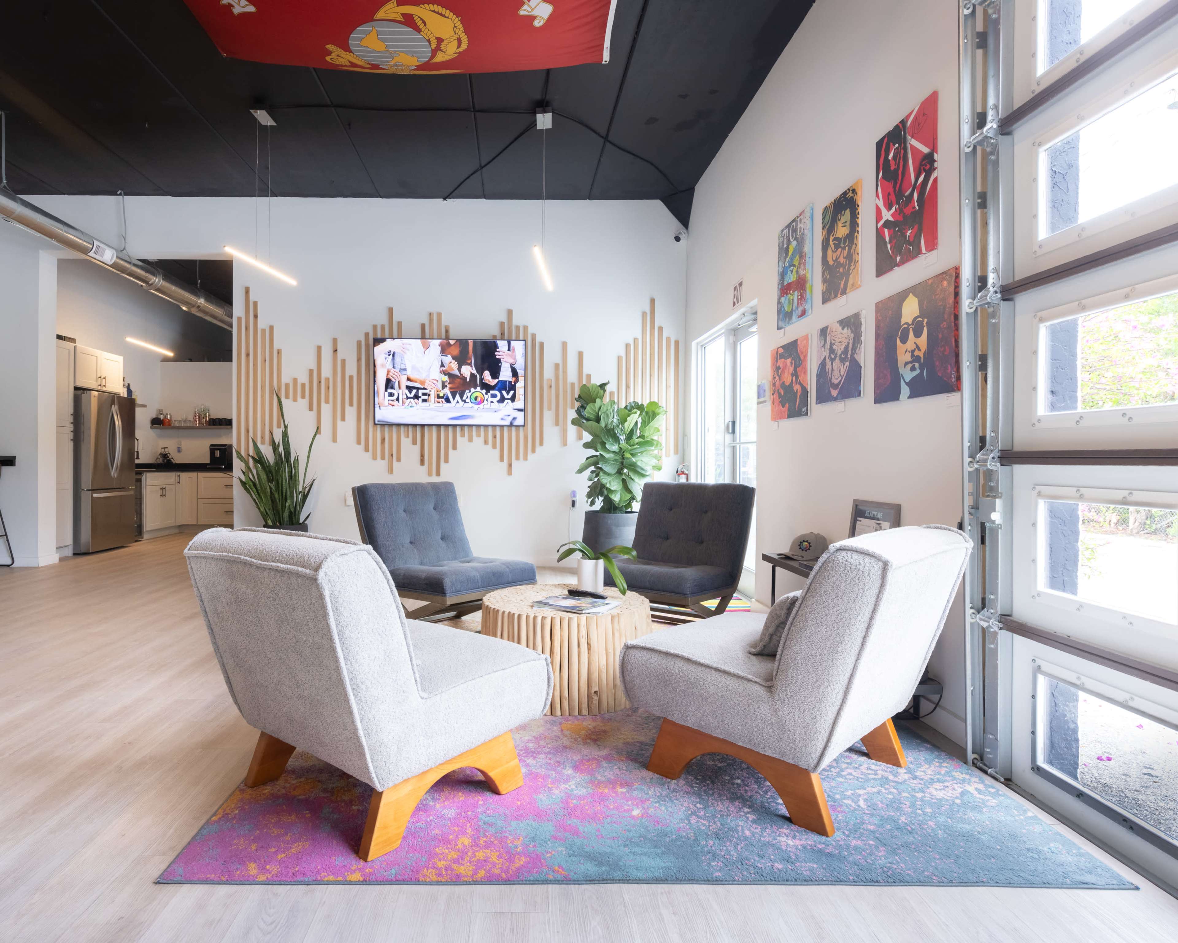 A modern lounge area features four armchairs arranged around a round wooden coffee table, with a flat-screen TV mounted on the wall and framed artwork displayed nearby.