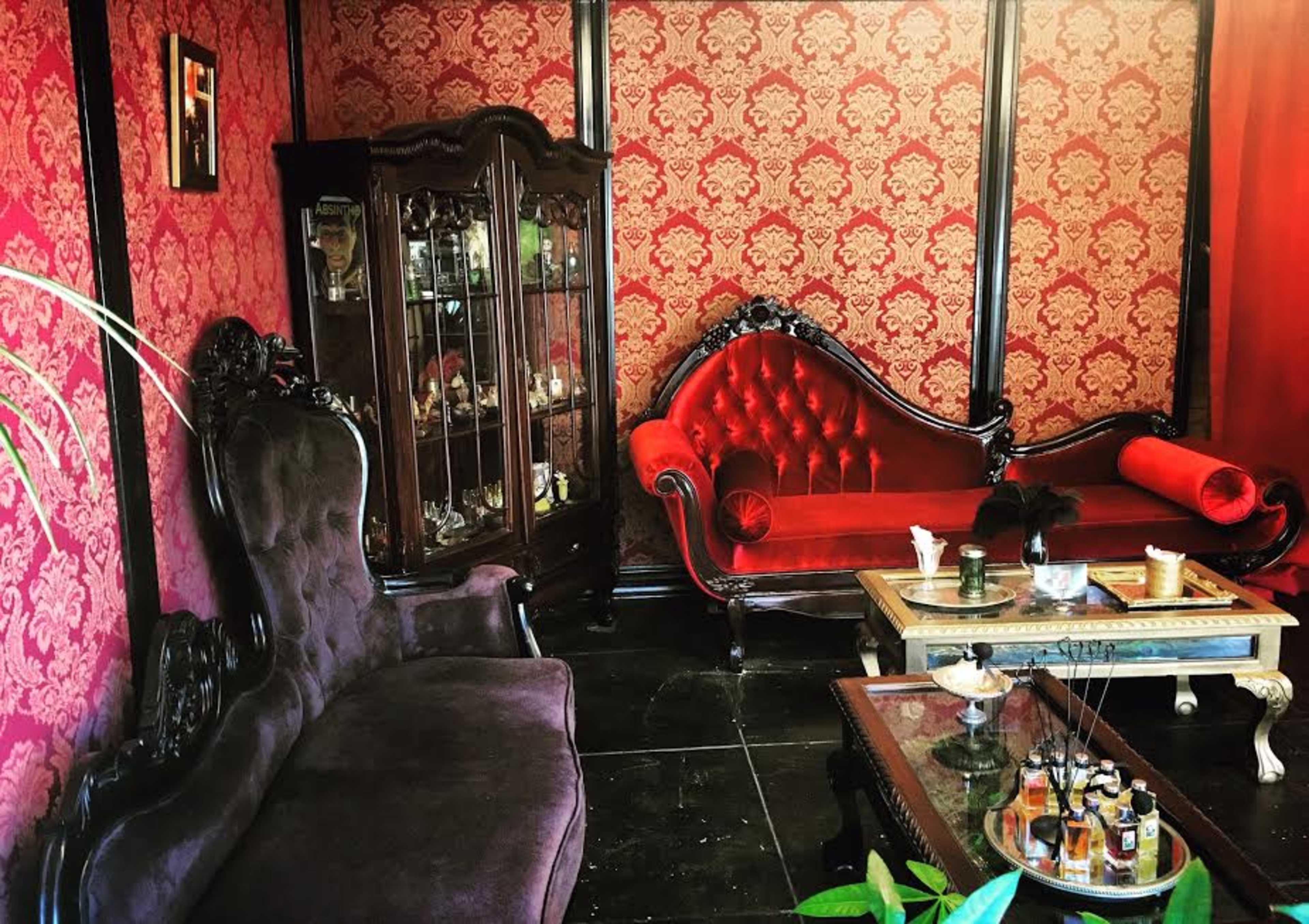 The room features ornate red wallpaper with a vintage furniture arrangement, including a plush burgundy sofa, a dark purple couch, and a wooden display cabinet.