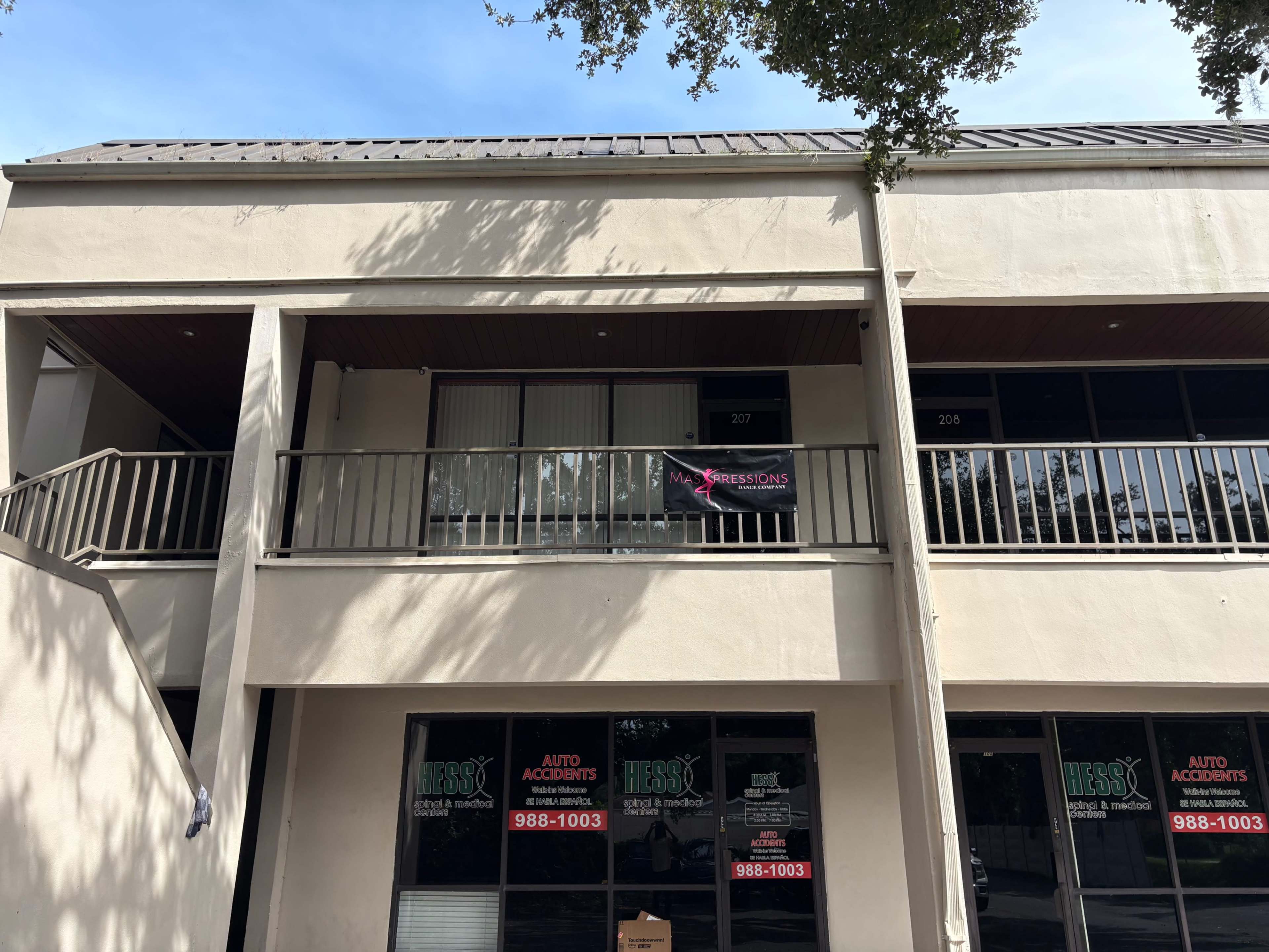 The image shows a two-story building with a balcony on the upper level and a sign hanging on the balcony, while ground-level storefronts display signs for auto accident services.