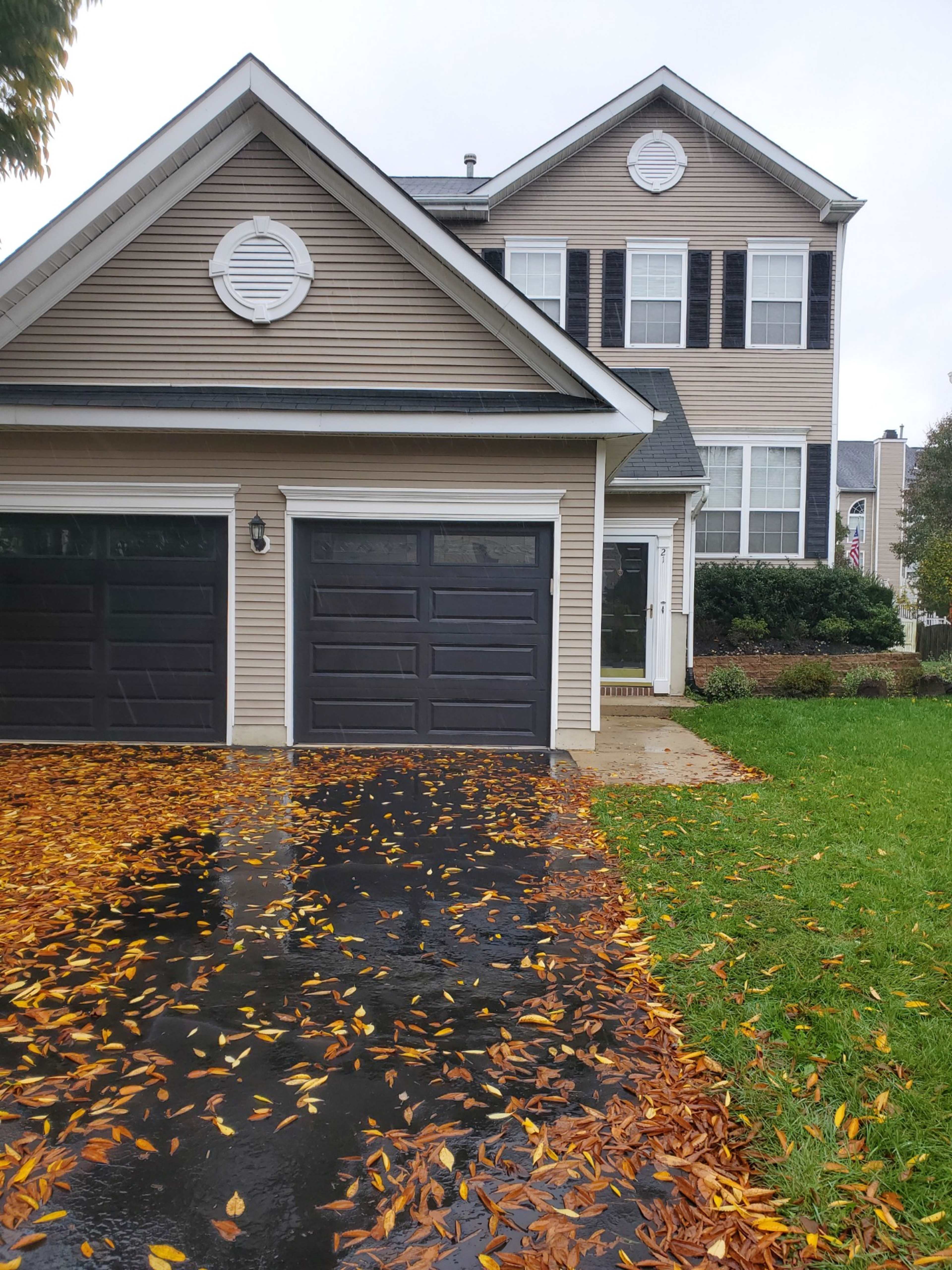 A two-story house with a front porch and a driveway covered in fallen leaves.