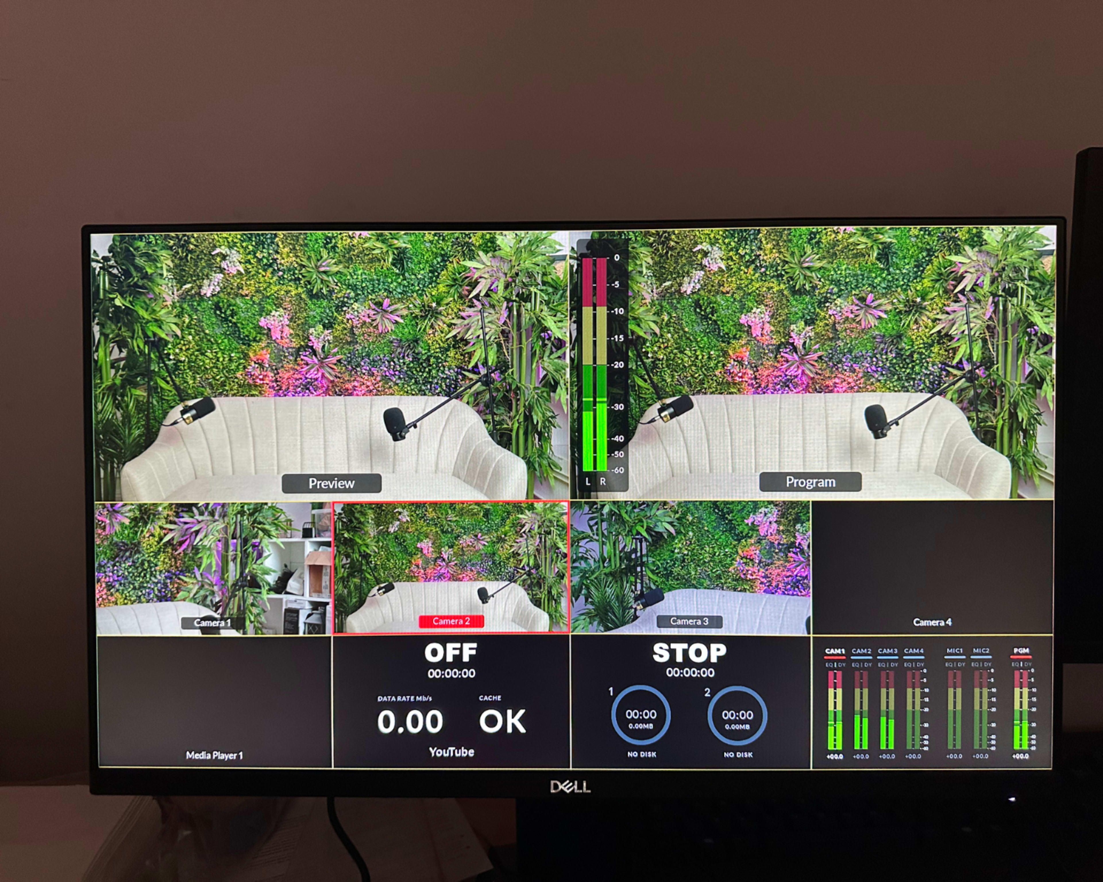 The image displays a monitor with a multi-camera setup for a video production, featuring a preview and program view alongside audio levels and broadcast controls.