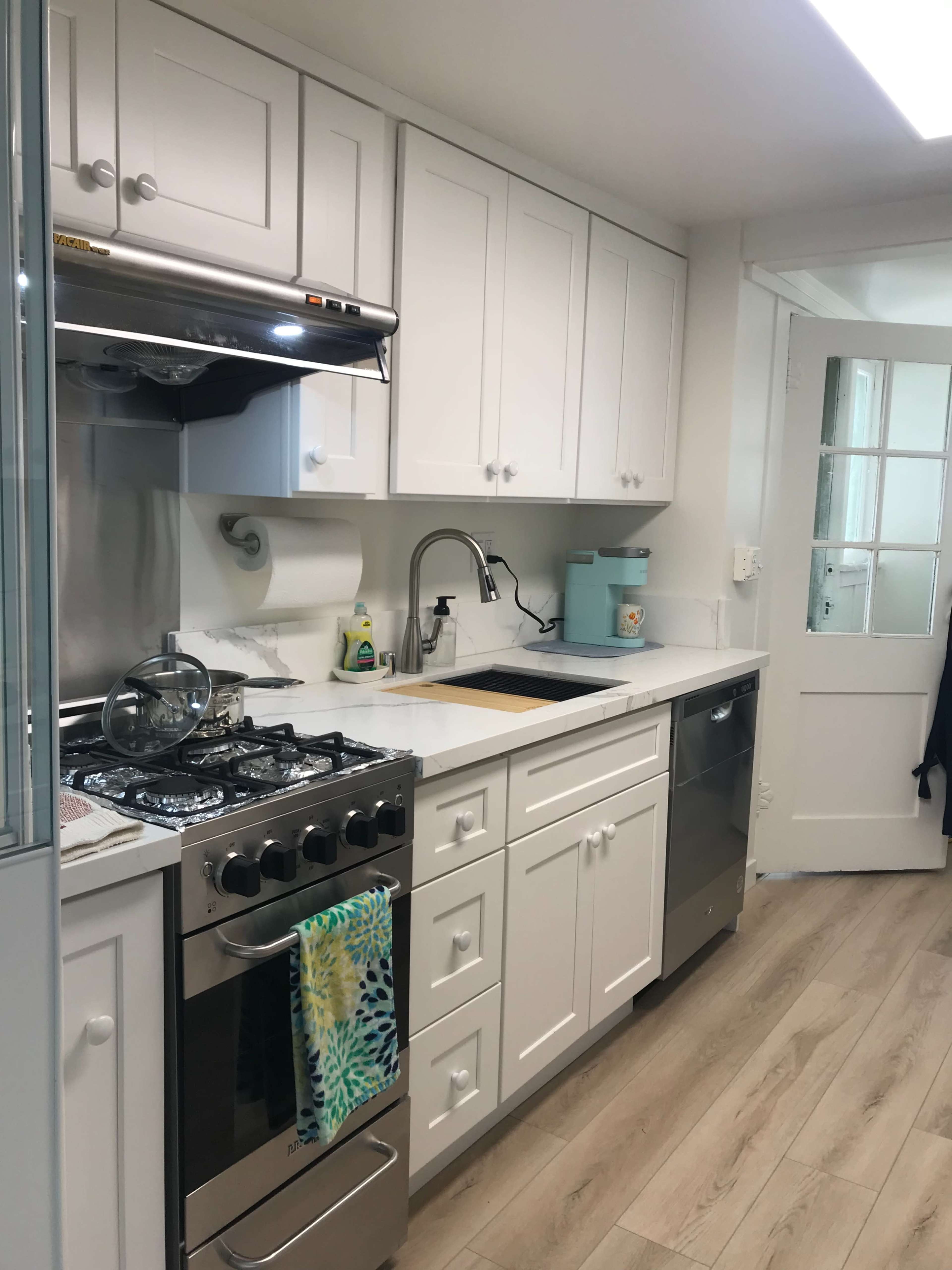 A compact kitchen features white cabinets, a stainless steel stove, and a sink with a modern faucet, alongside a dishwasher and a door leading to another room.