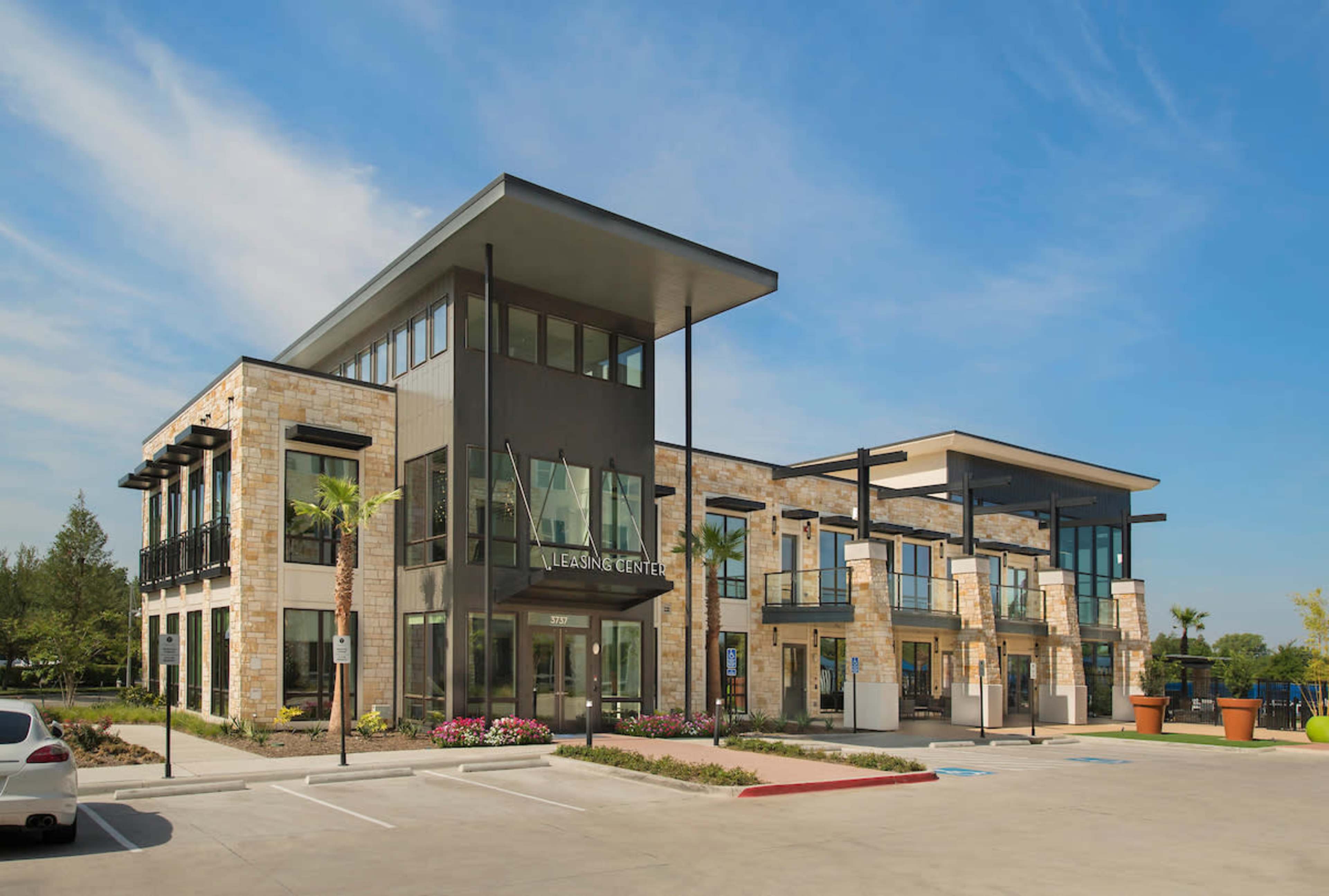 A modern two-story commercial building features large glass windows, a stone facade, and palm trees in the surrounding landscaping.