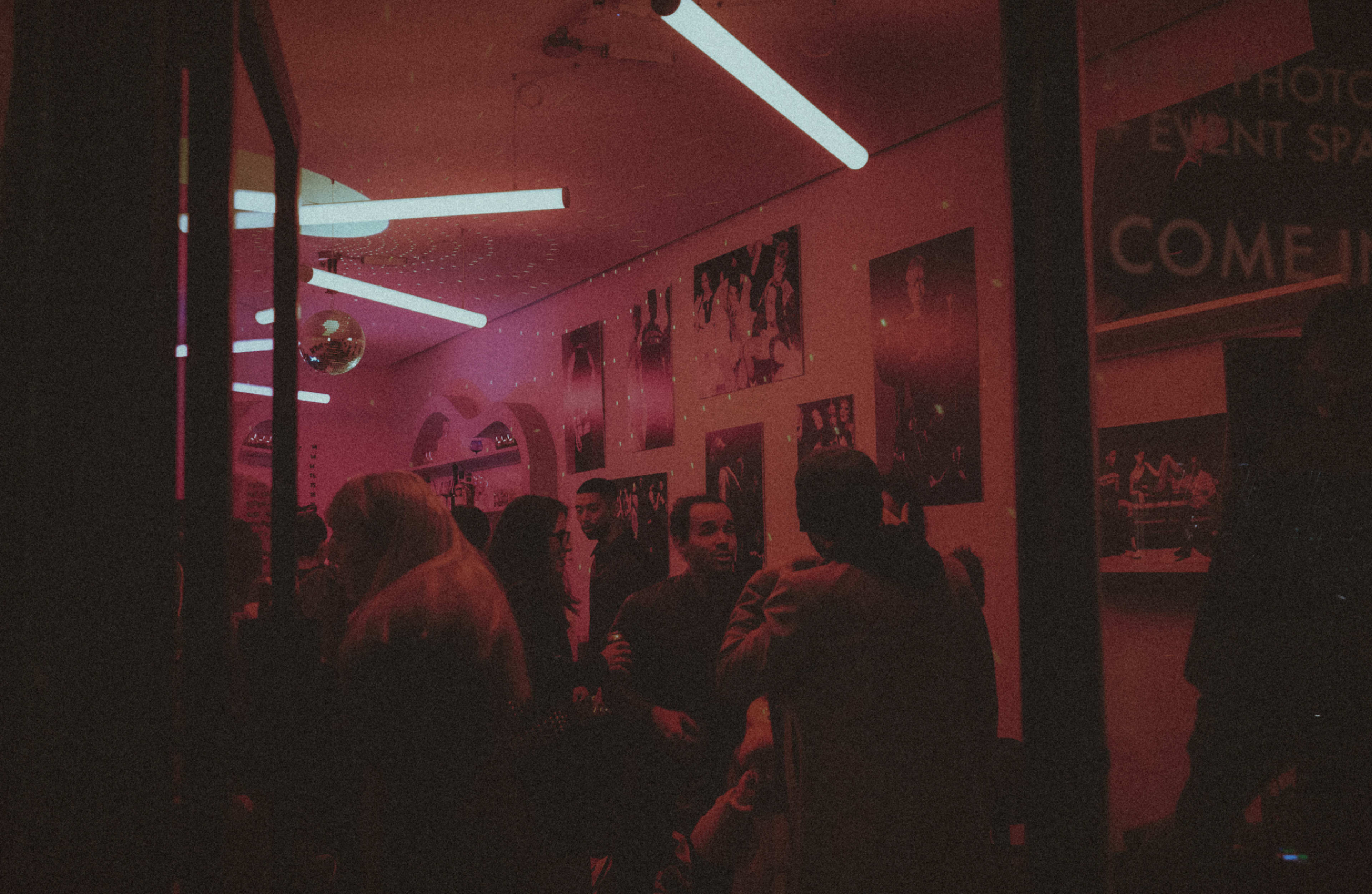 A group of people socialize in a dimly lit room adorned with artwork and illuminated by neon lights.
