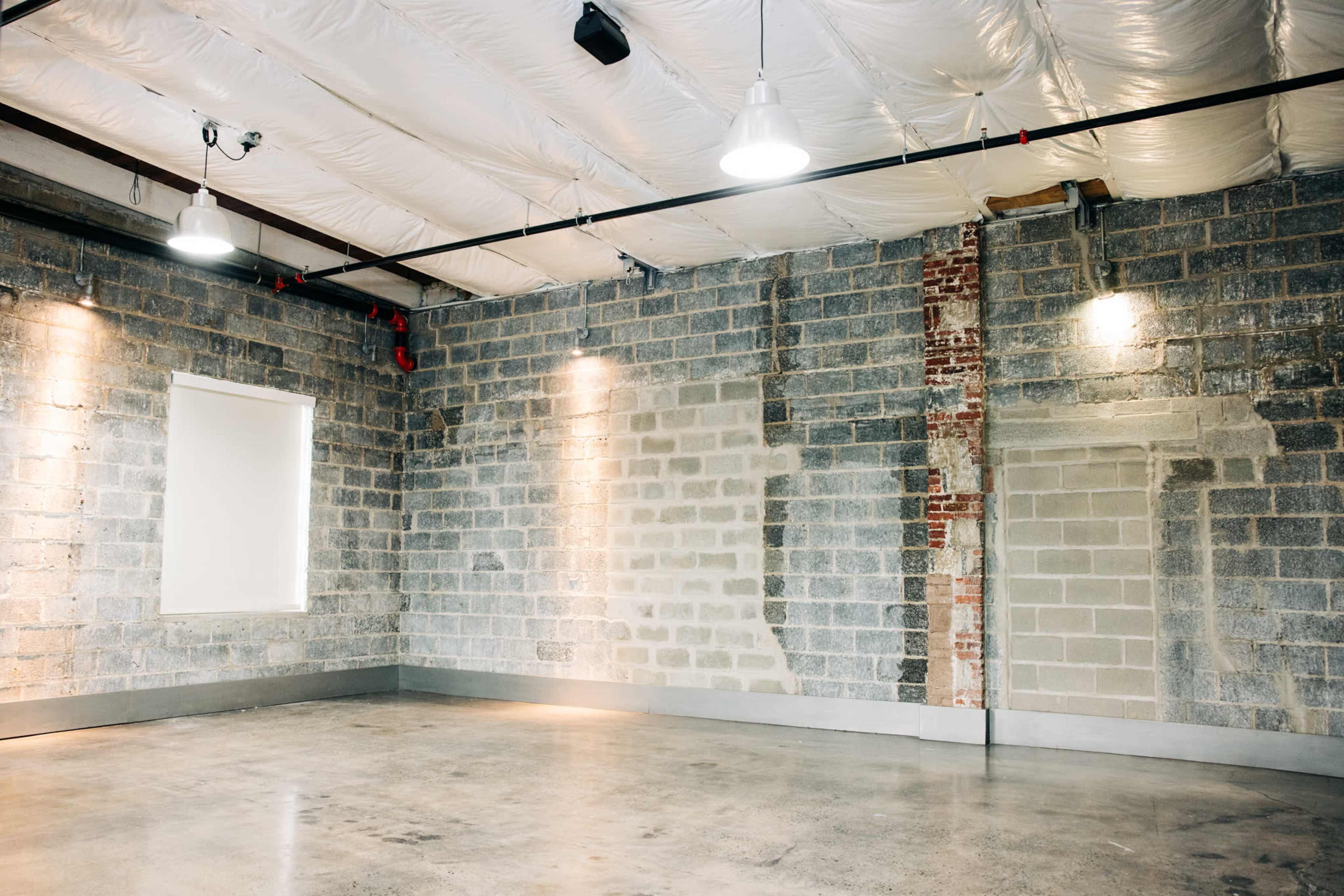 The image shows an empty industrial space with gray concrete walls, a polished floor, and ceiling-mounted lights.