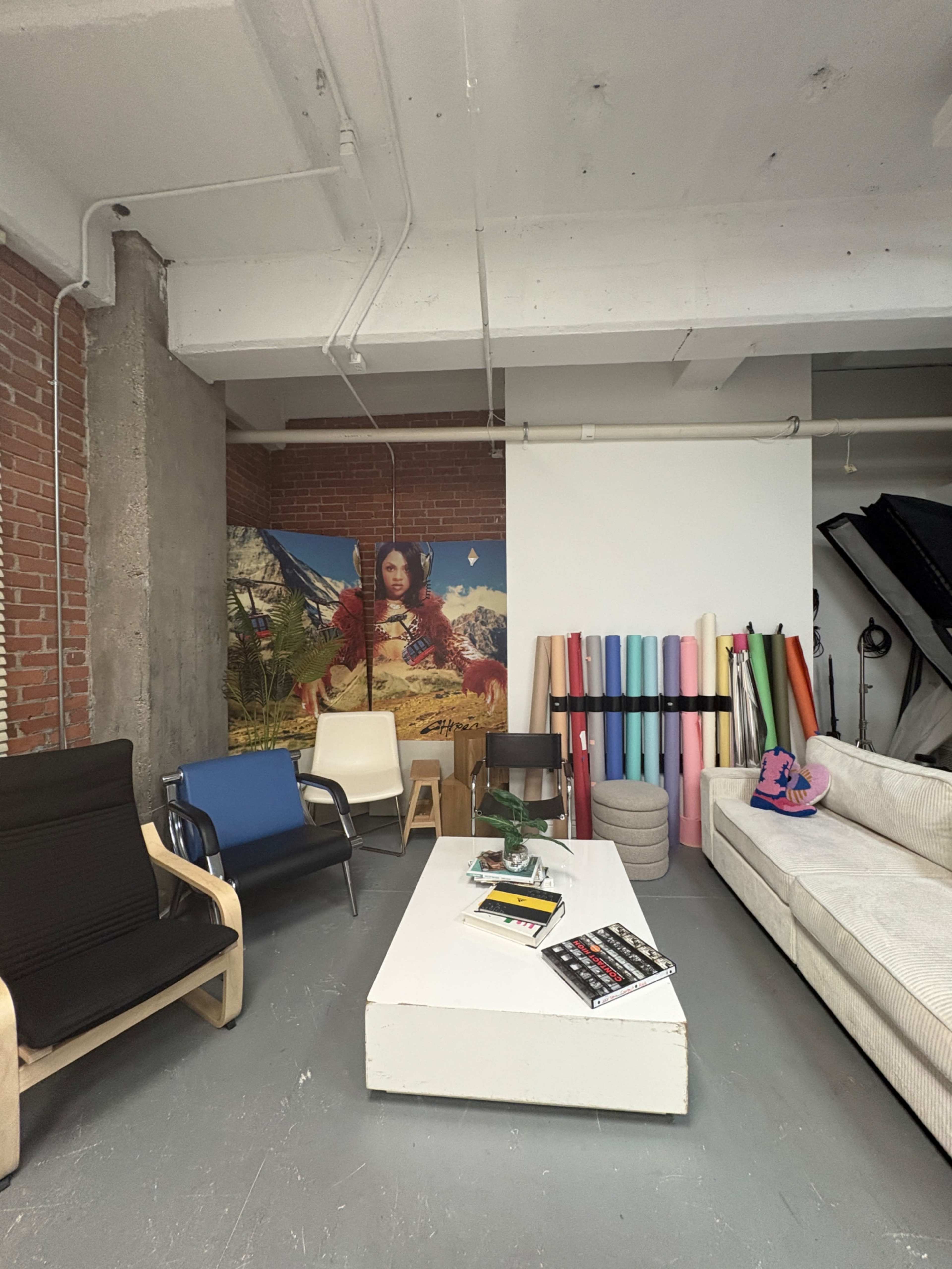 The image shows a spacious studio area with a mix of colorful backdrops, various seating arrangements, and rolls of colorful materials against the wall.