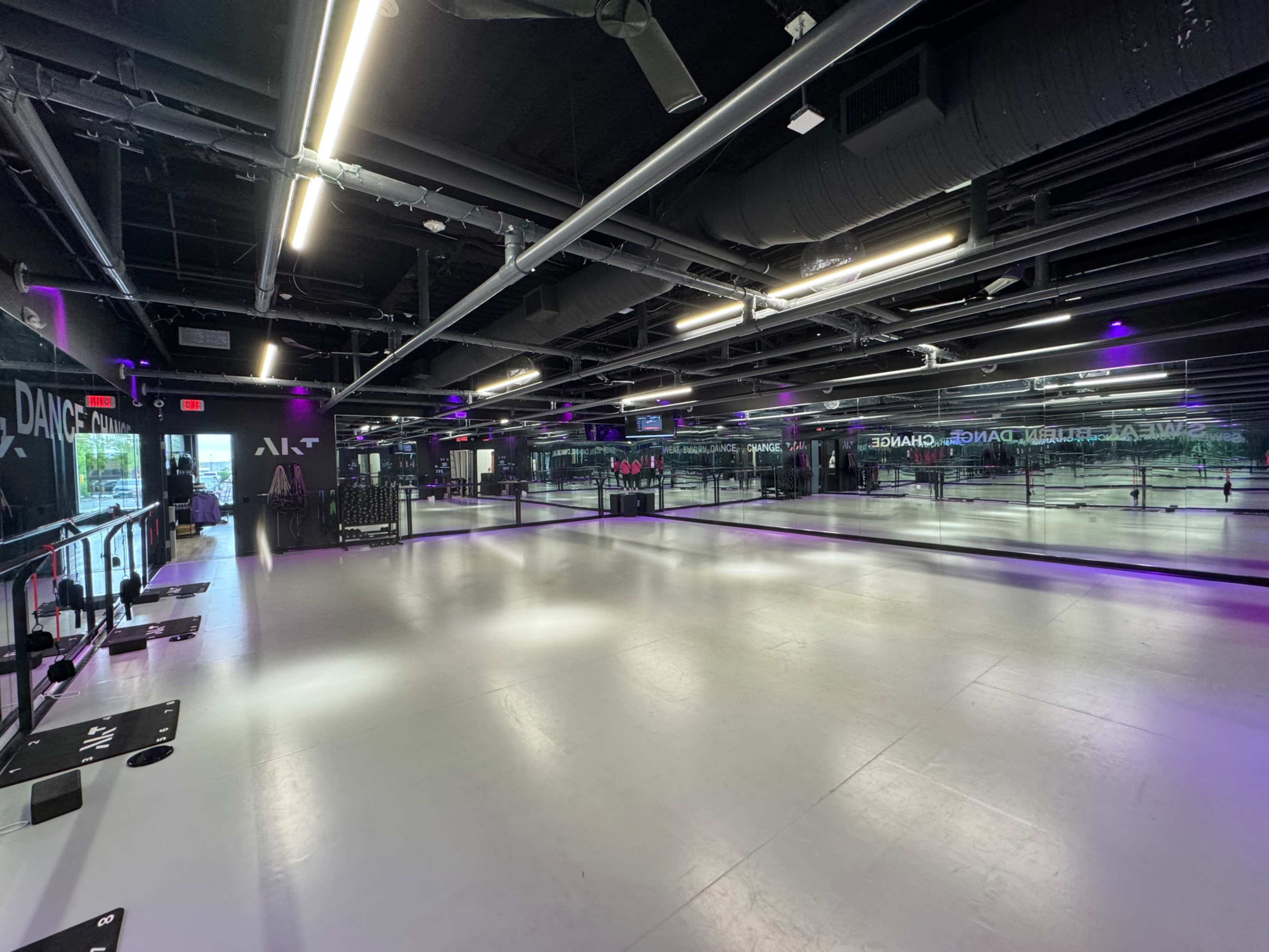 A spacious dance studio with mirrored walls, a smooth white floor, and purple lighting.