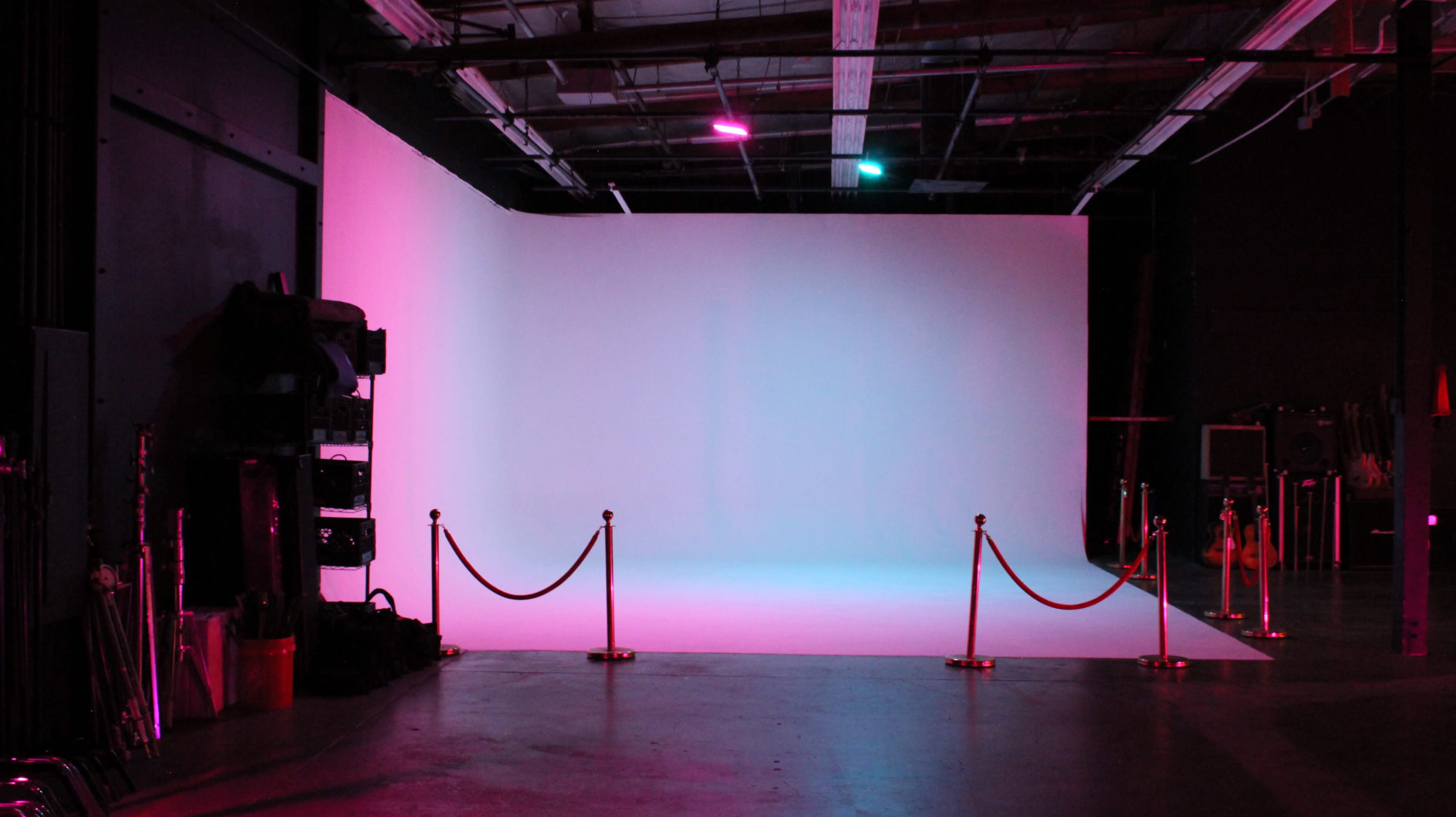 The image depicts a spacious studio with a gradient light backdrop and velvet ropes delineating a designated area.