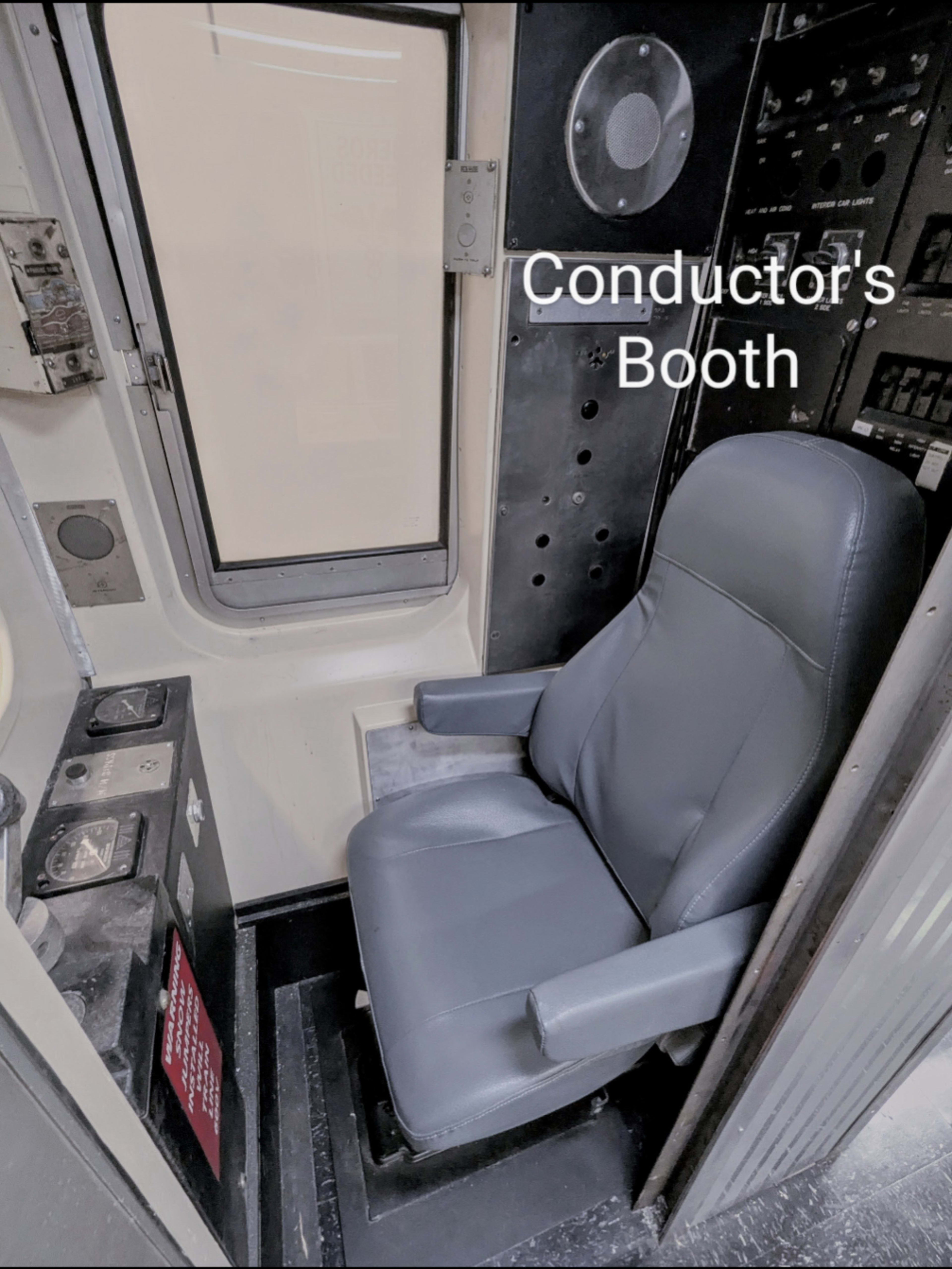 The image shows a conductor's booth featuring a chair, control panel, and large window.