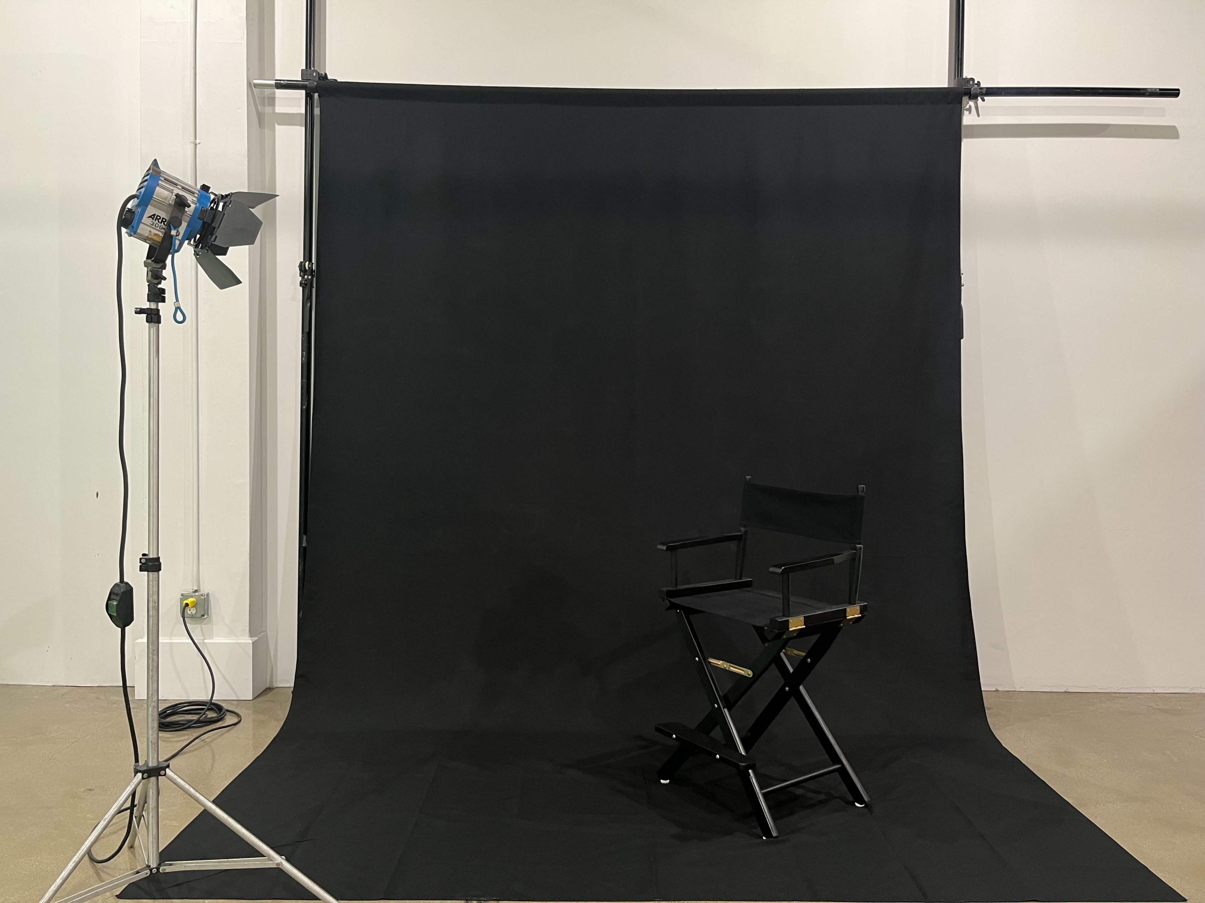A black backdrop is set up in a photography studio with a director's chair and a spotlight positioned nearby.