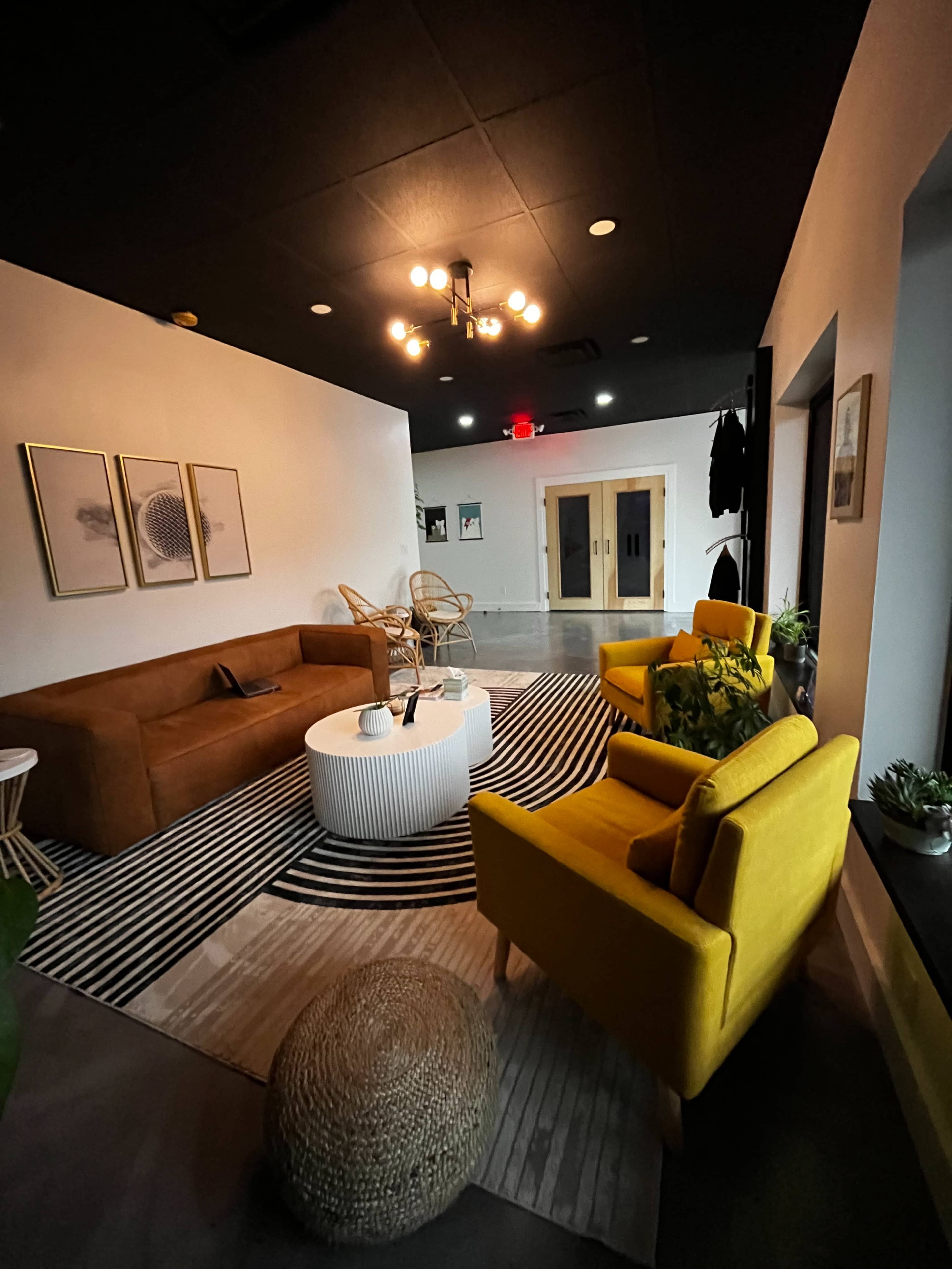 The image shows a modern living space featuring a brown leather sofa, yellow armchairs, a round white coffee table, and patterned rugs.
