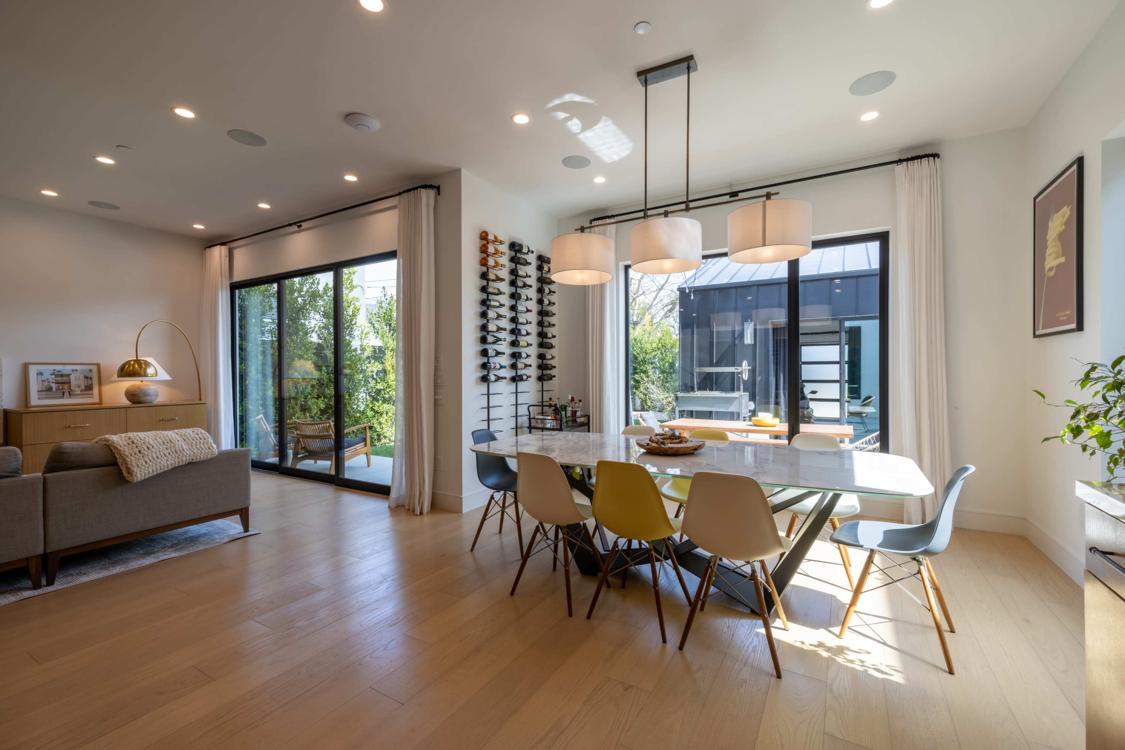 A dining area features a marble table surrounded by multi-colored chairs and large windows that open to an outdoor space.