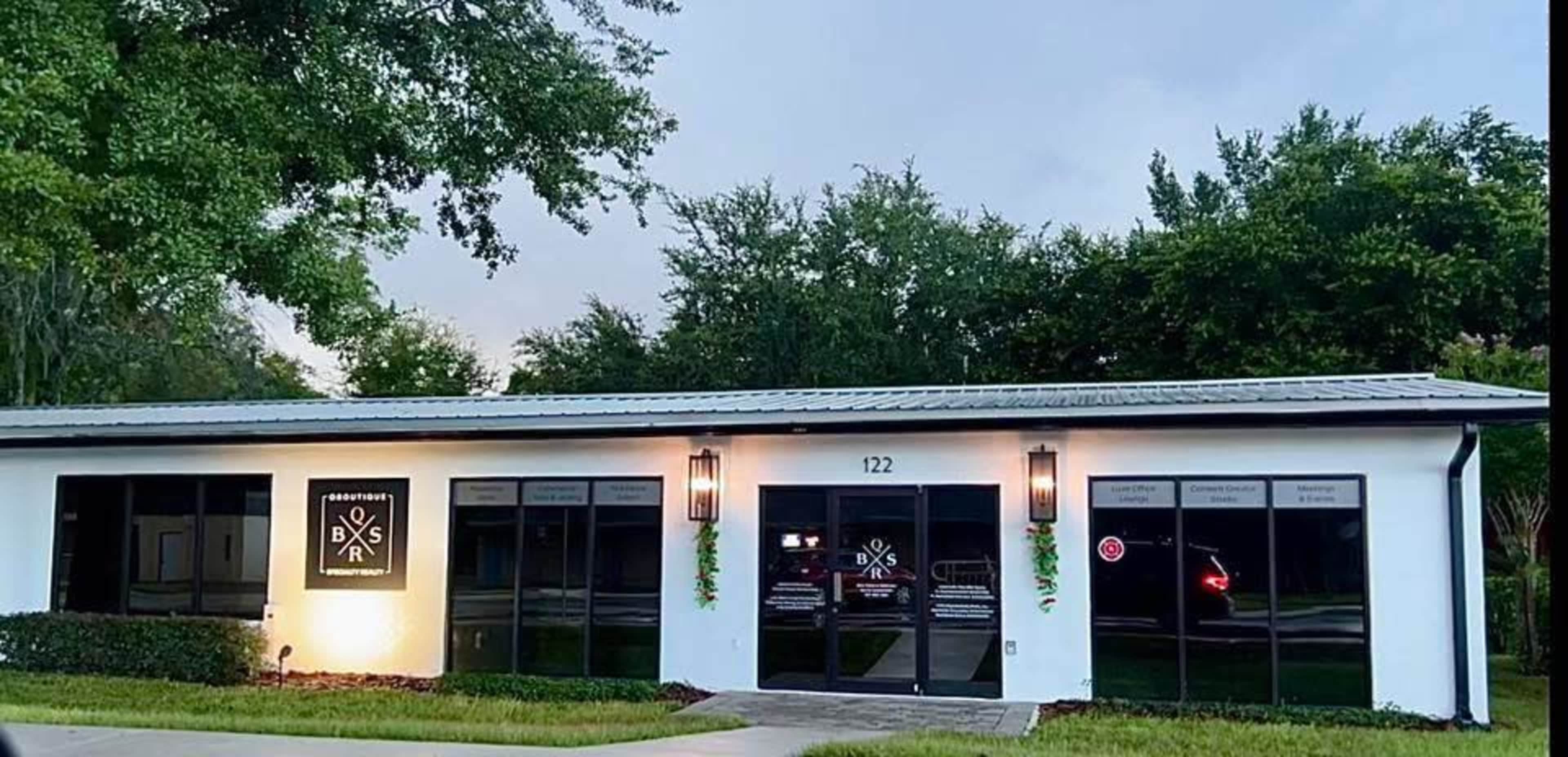 The image shows a modern, single-story commercial building with a flat roof and large windows, featuring a sign that reads "BXS" on the front wall.