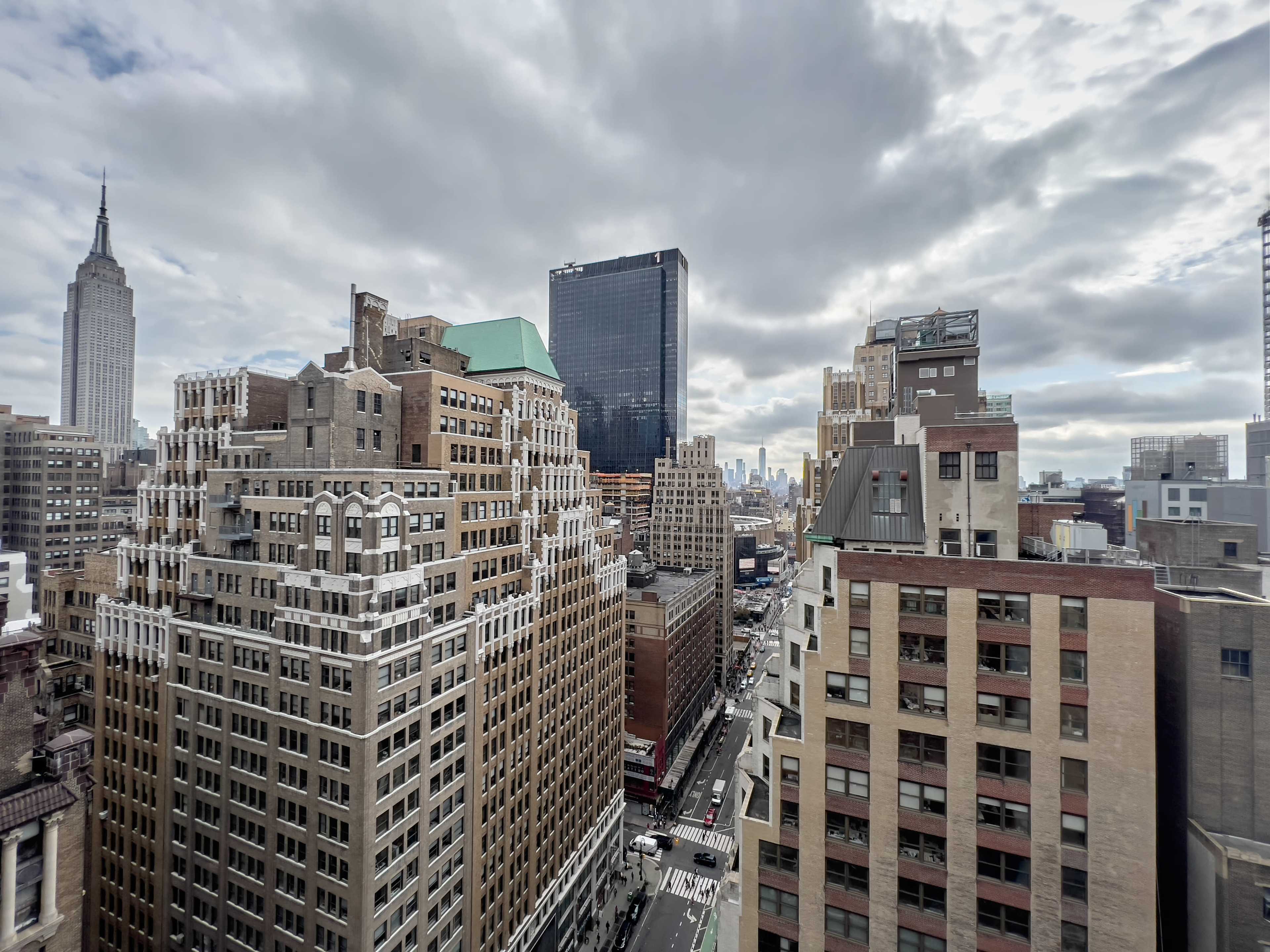A view of New York City, featuring the Empire State Building among various skyscrapers under a cloudy sky.