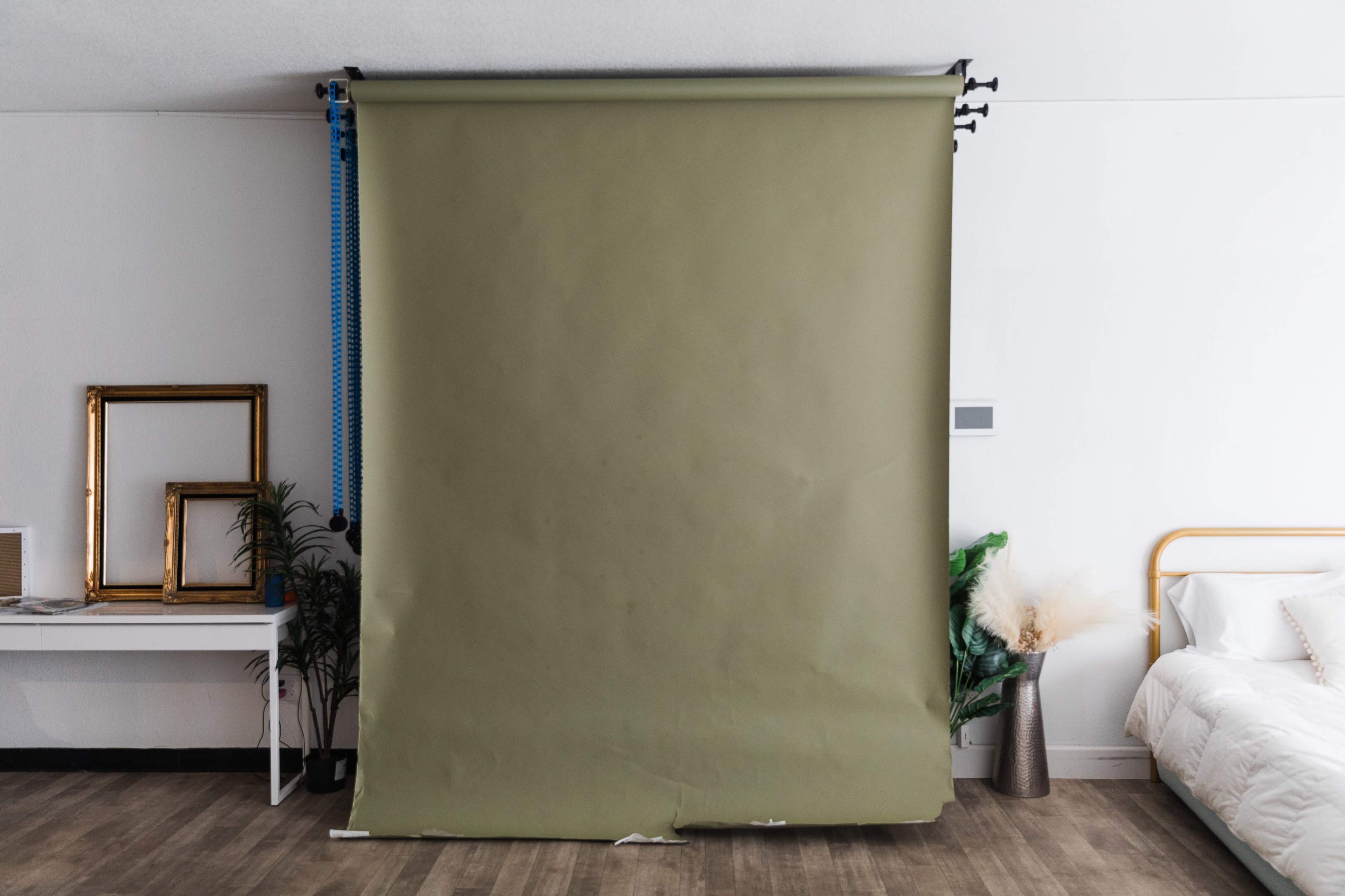 A minimalistic room featuring a green backdrop, a white bed, a small table with a framed picture, and decorative plants.