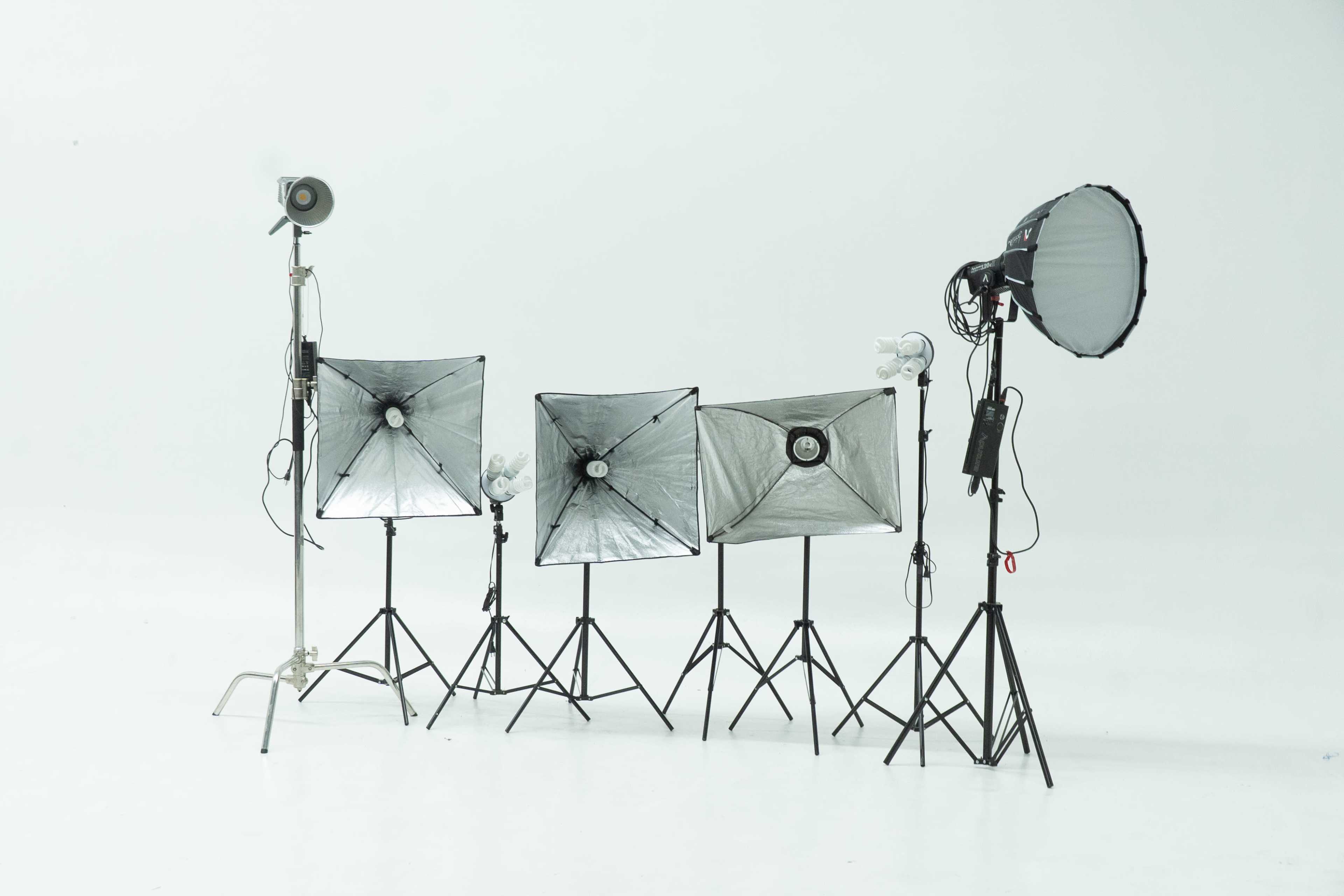 A collection of photography lighting equipment, including softboxes and a spotlight, stands on tripods against a white backdrop.