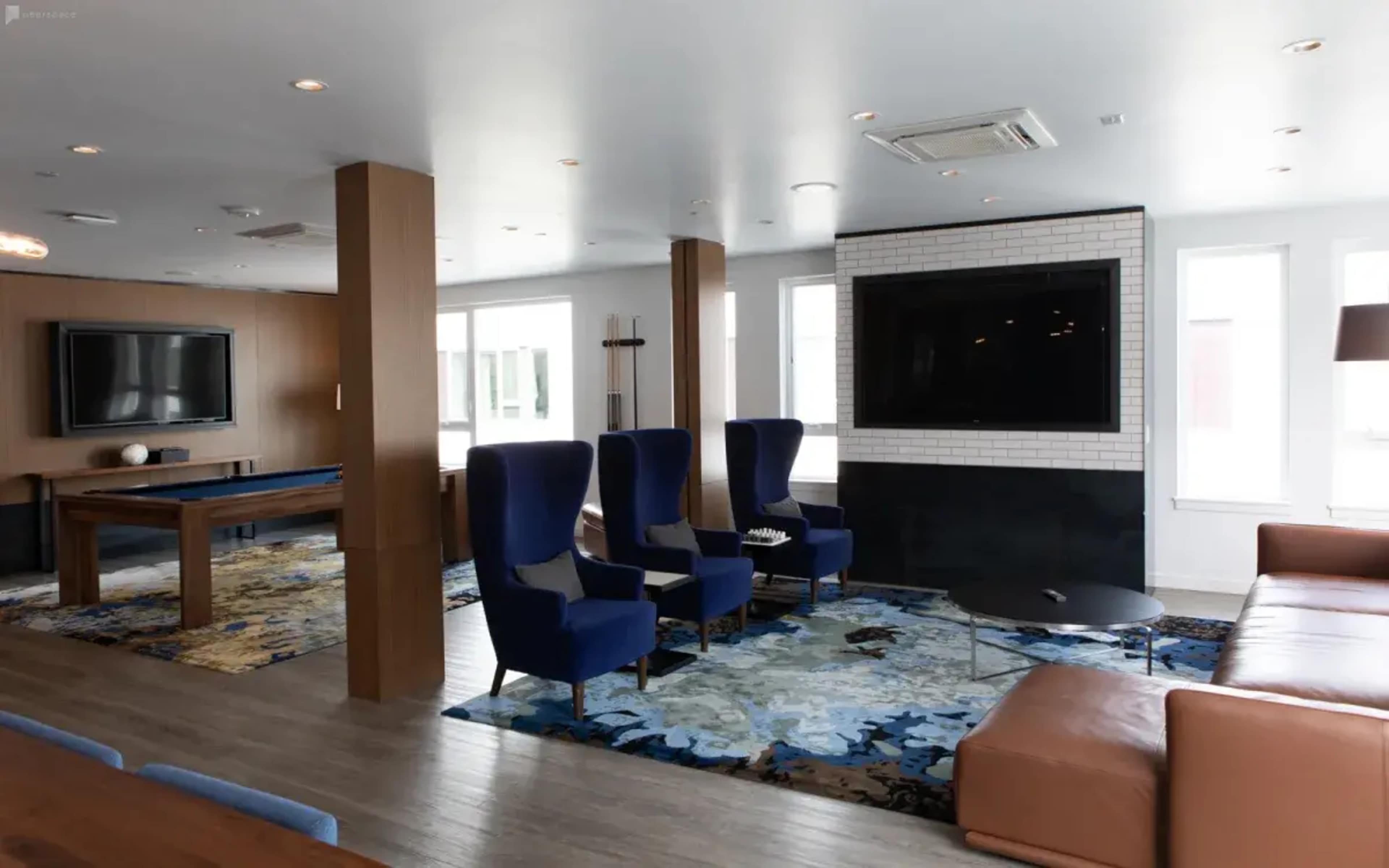 A modern living space with a sectional sofa, two armchairs, a coffee table, a television mounted on the wall, and large windows.