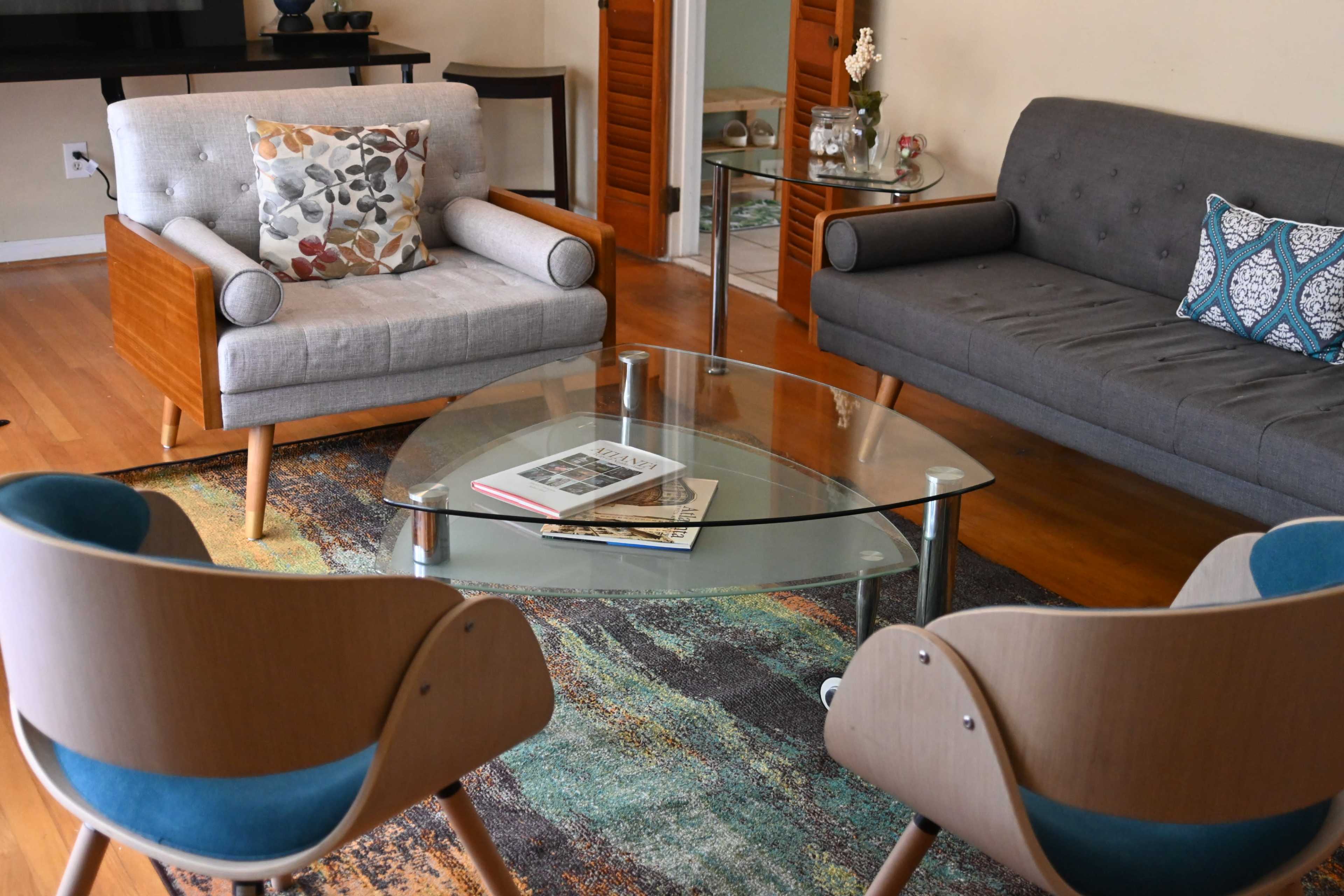 A living room with a glass coffee table surrounded by modern armchairs and a gray sofa, all set on a patterned rug.