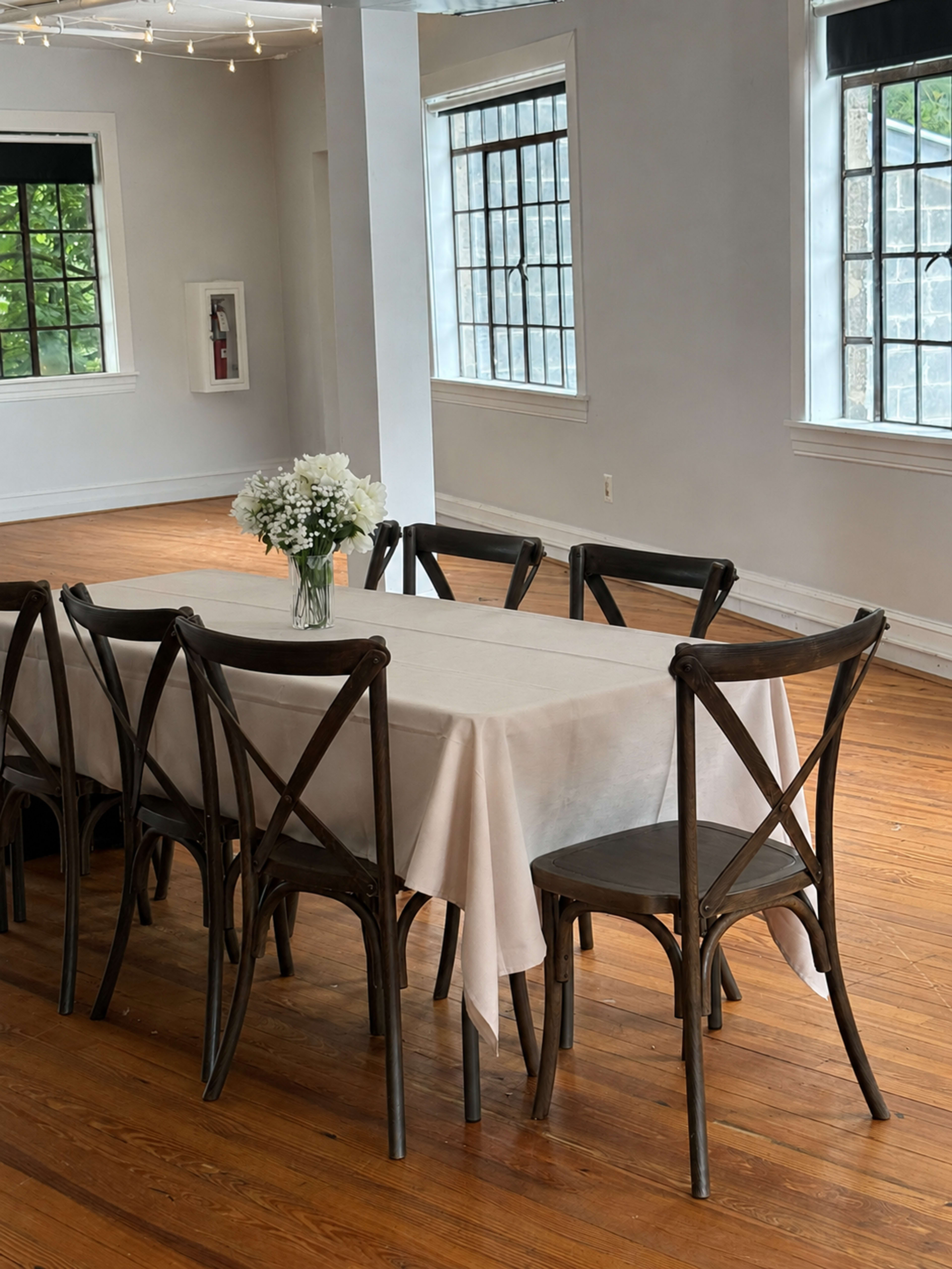 A long table covered with a light-colored cloth is set in a spacious room with wooden floors and large windows.