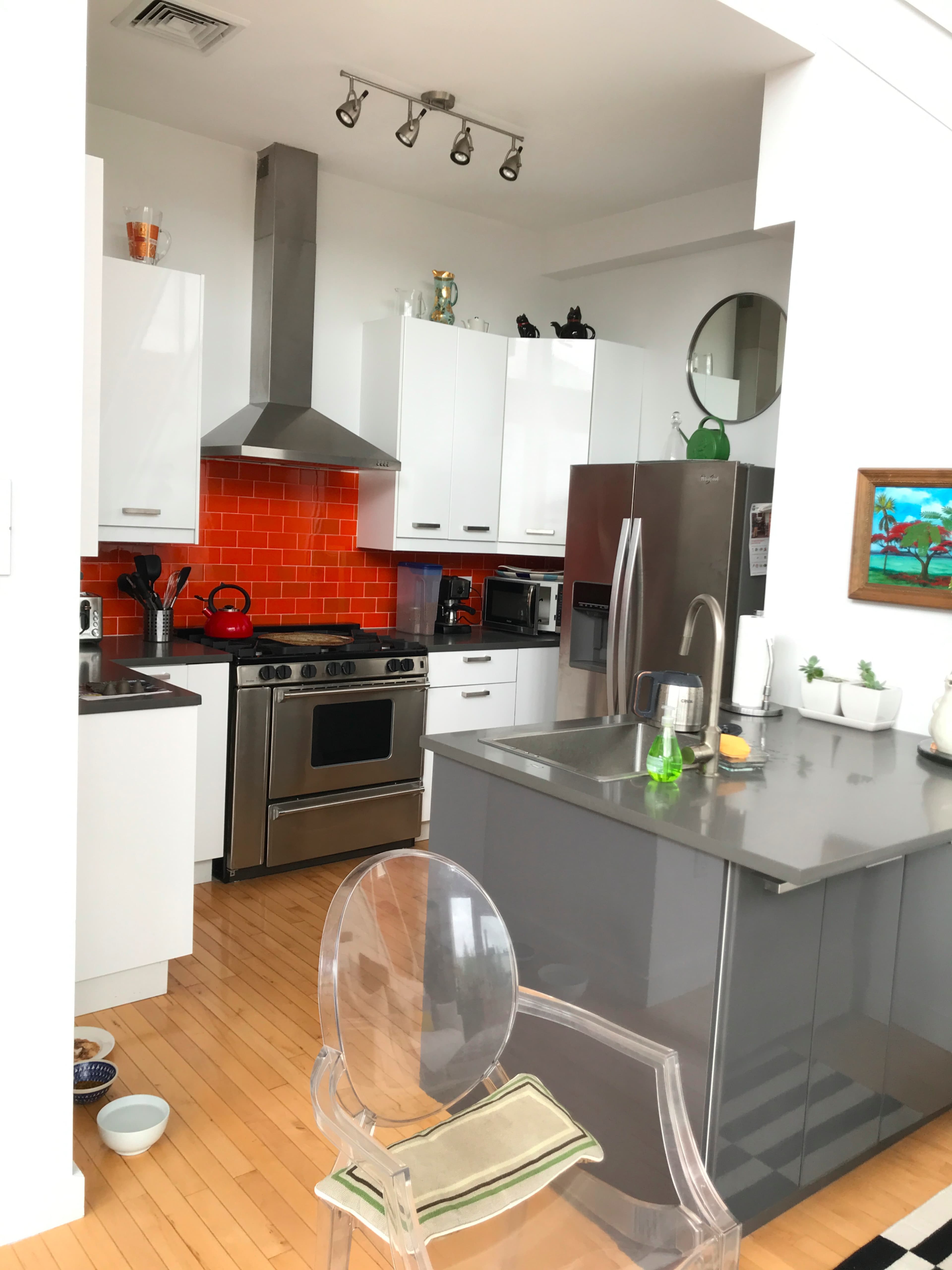 A modern kitchen features white cabinetry, a stainless steel oven, and an orange tiled backsplash.