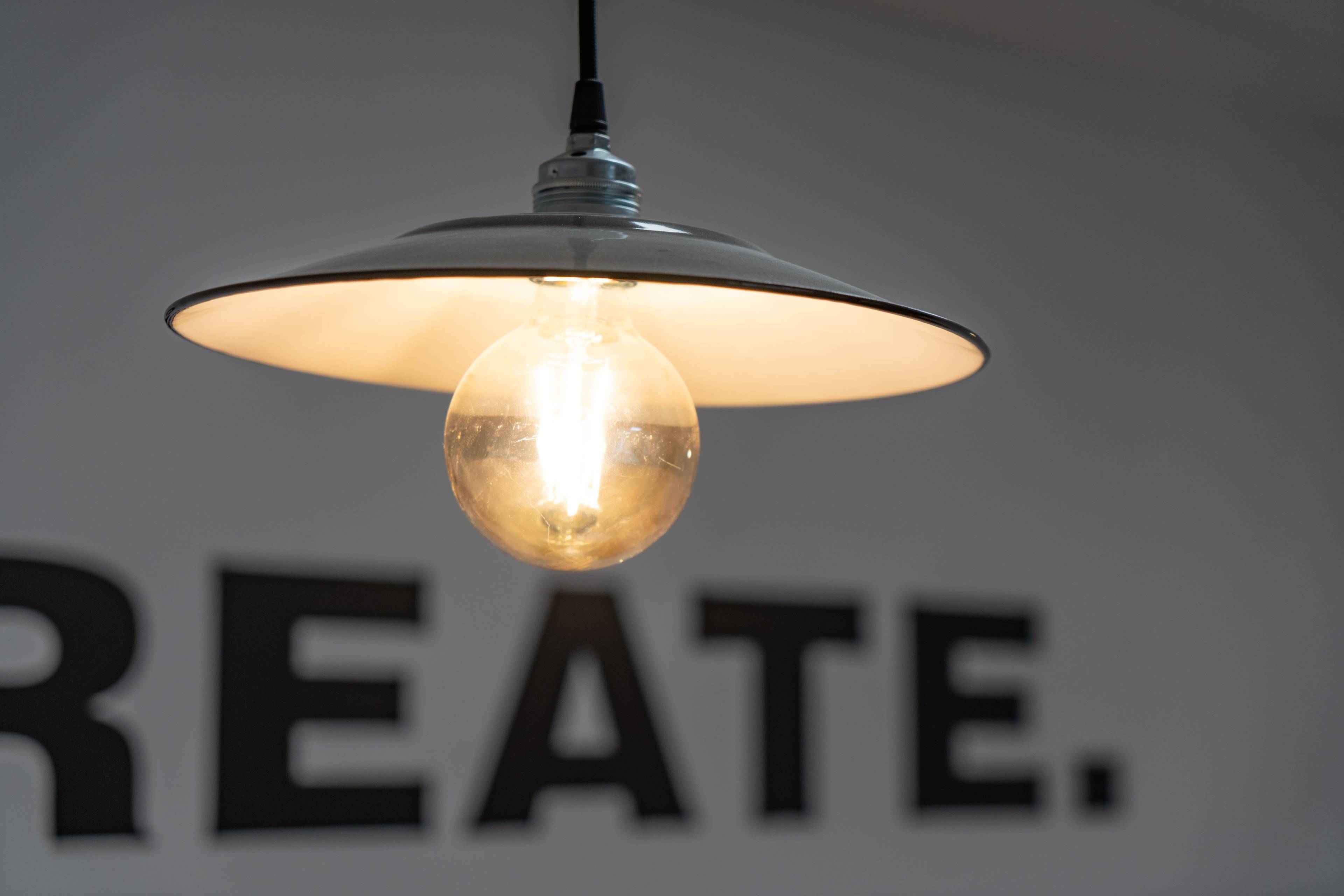 A pendant light with a clear bulb hangs above a wall featuring the word "CREATE."