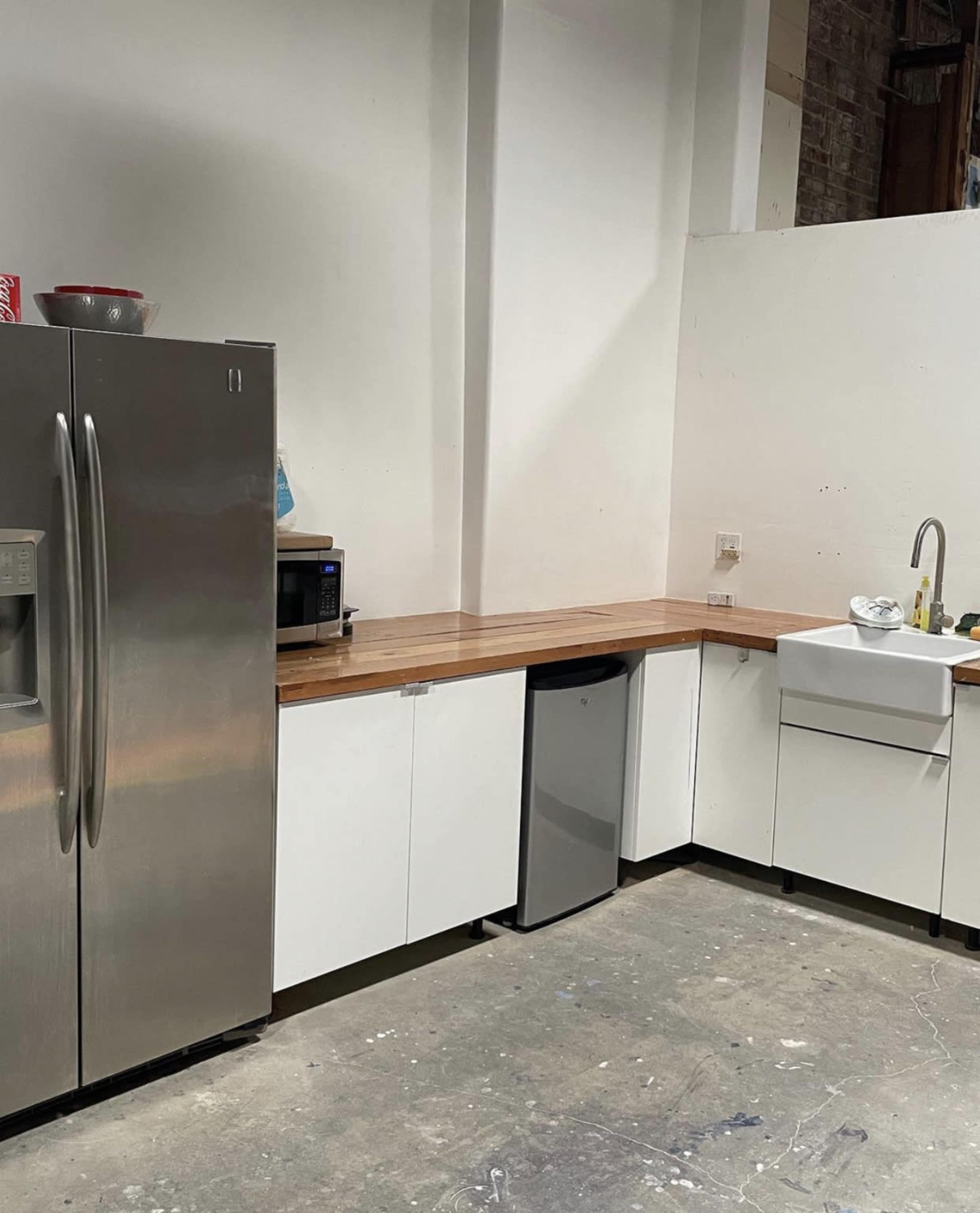 A kitchen area featuring a stainless steel refrigerator, a microwave, a sink, and white cabinetry with a wooden countertop.