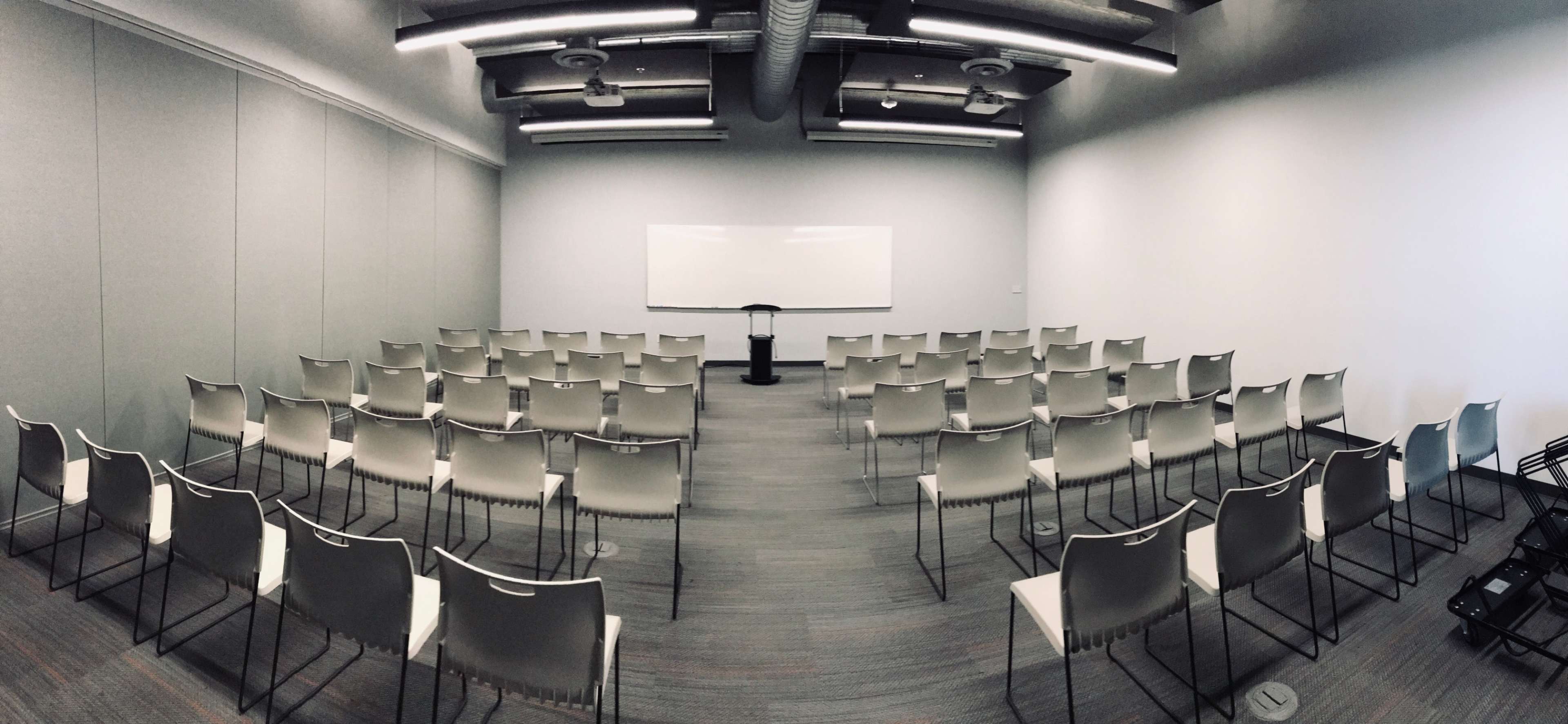 A conference room with rows of empty chairs facing a podium and whiteboard.