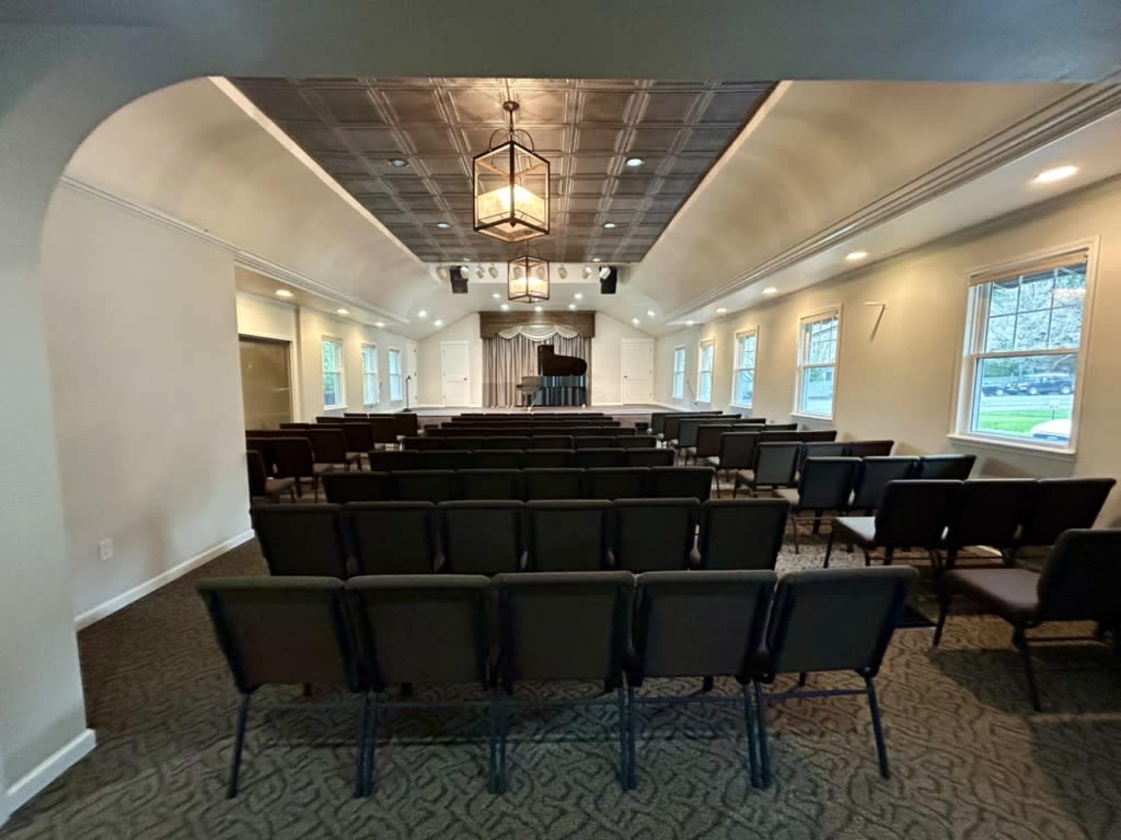 The image shows a spacious, well-lit hall set up with rows of chairs facing a stage with a podium and a backdrop.