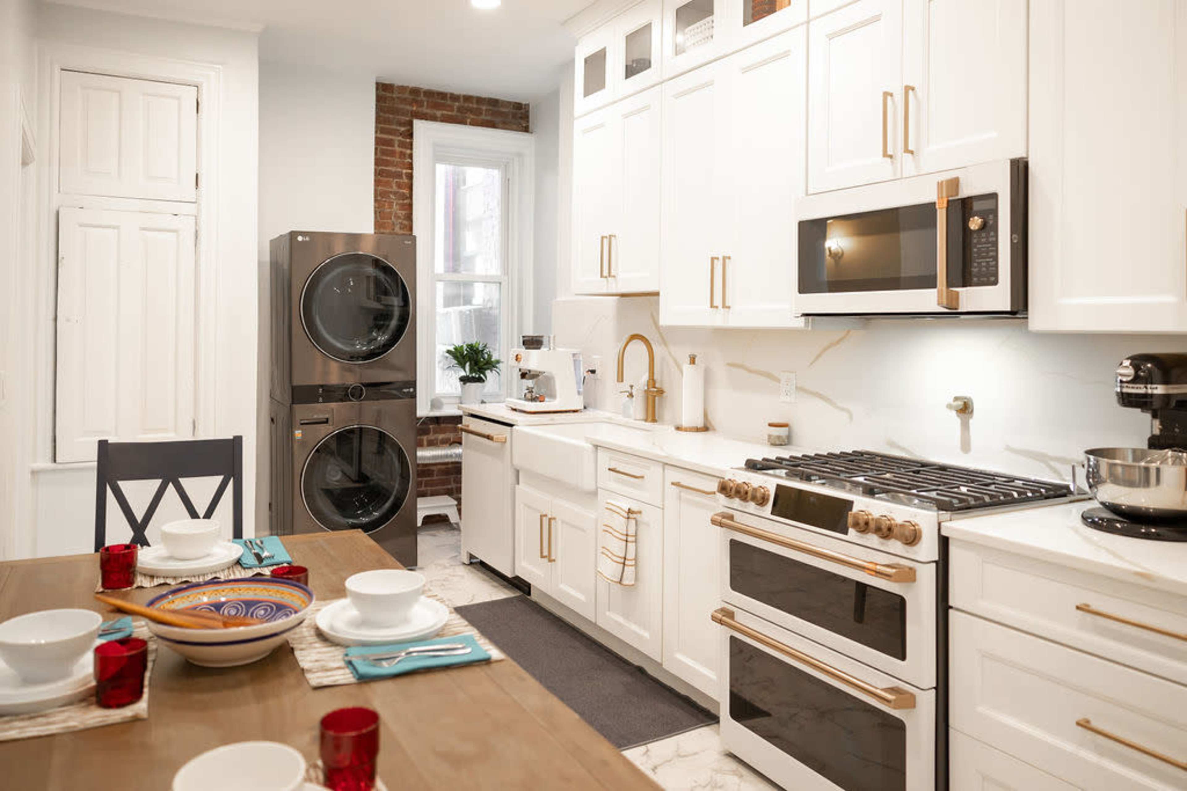 A modern kitchen with white cabinetry, stainless steel appliances, and a wooden dining table set for a meal.