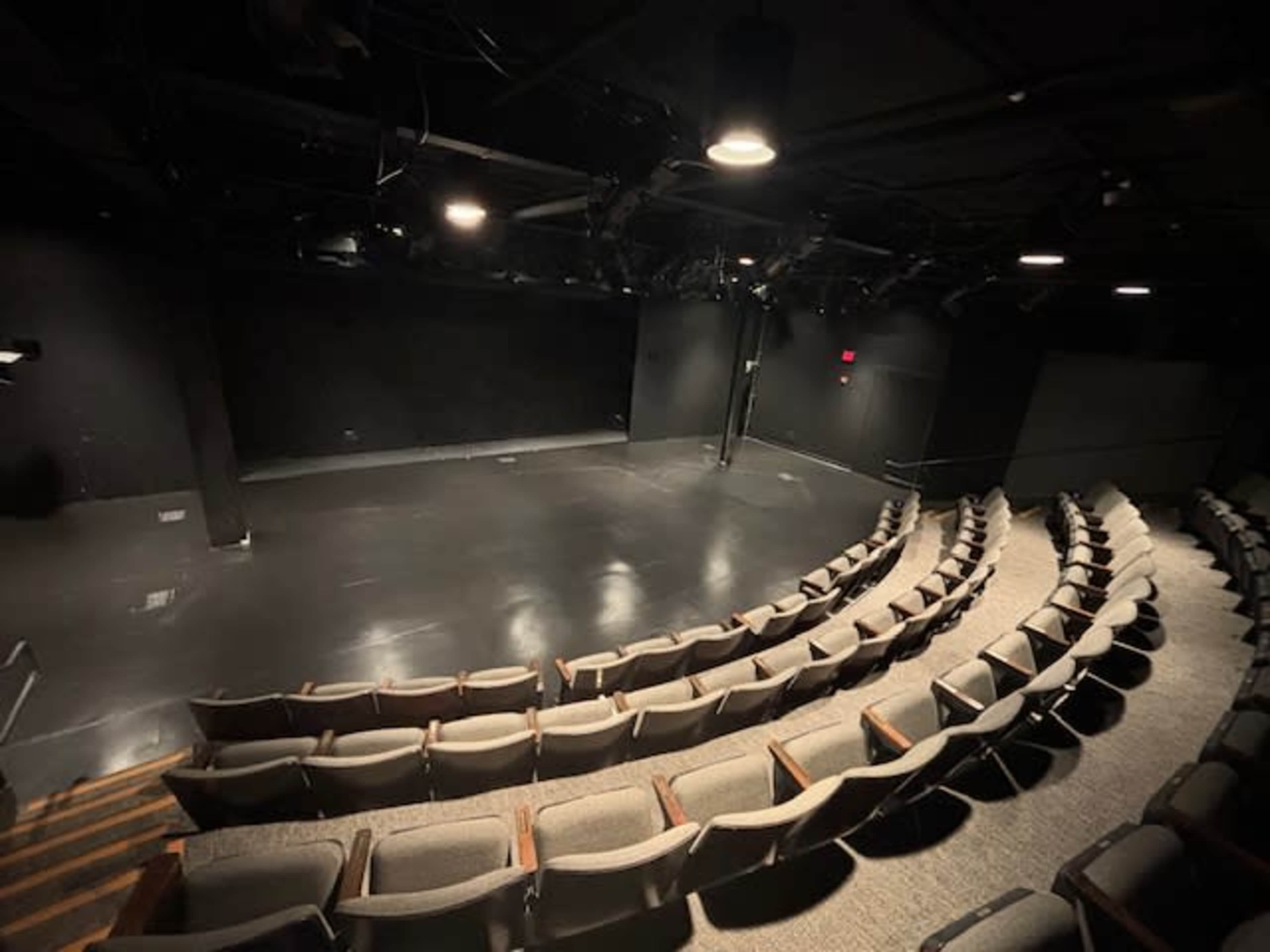 A black box theater with tiered seating and a clear performance stage at the front.